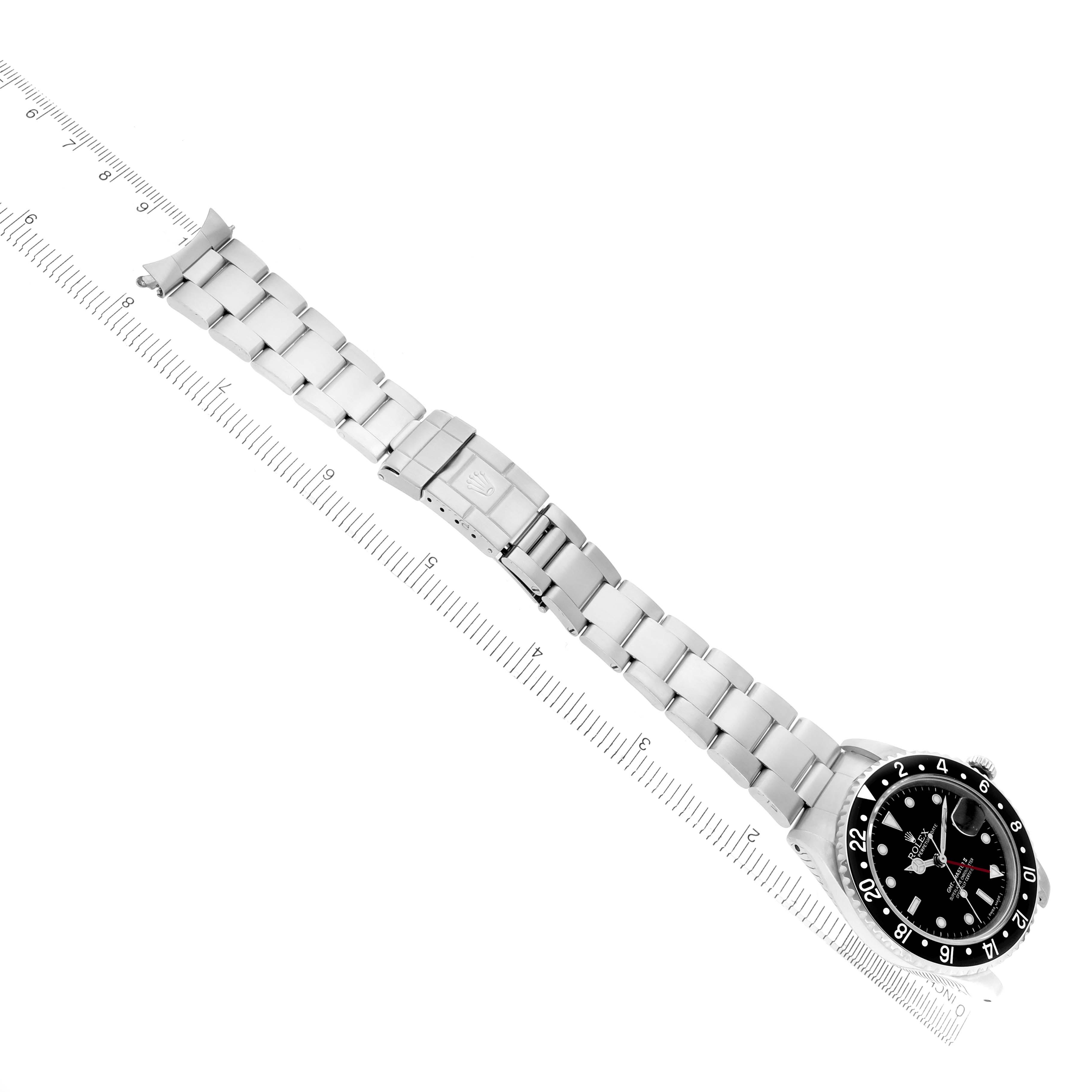 The Rolex GMT-Master 16710 Men
s Stainless Steel Black Dial 16710 Men
s Stainless Steel Black Dial watch is shown from a top-down angle, displaying the full bracelet, clasp, and face with a ruler beside it.
