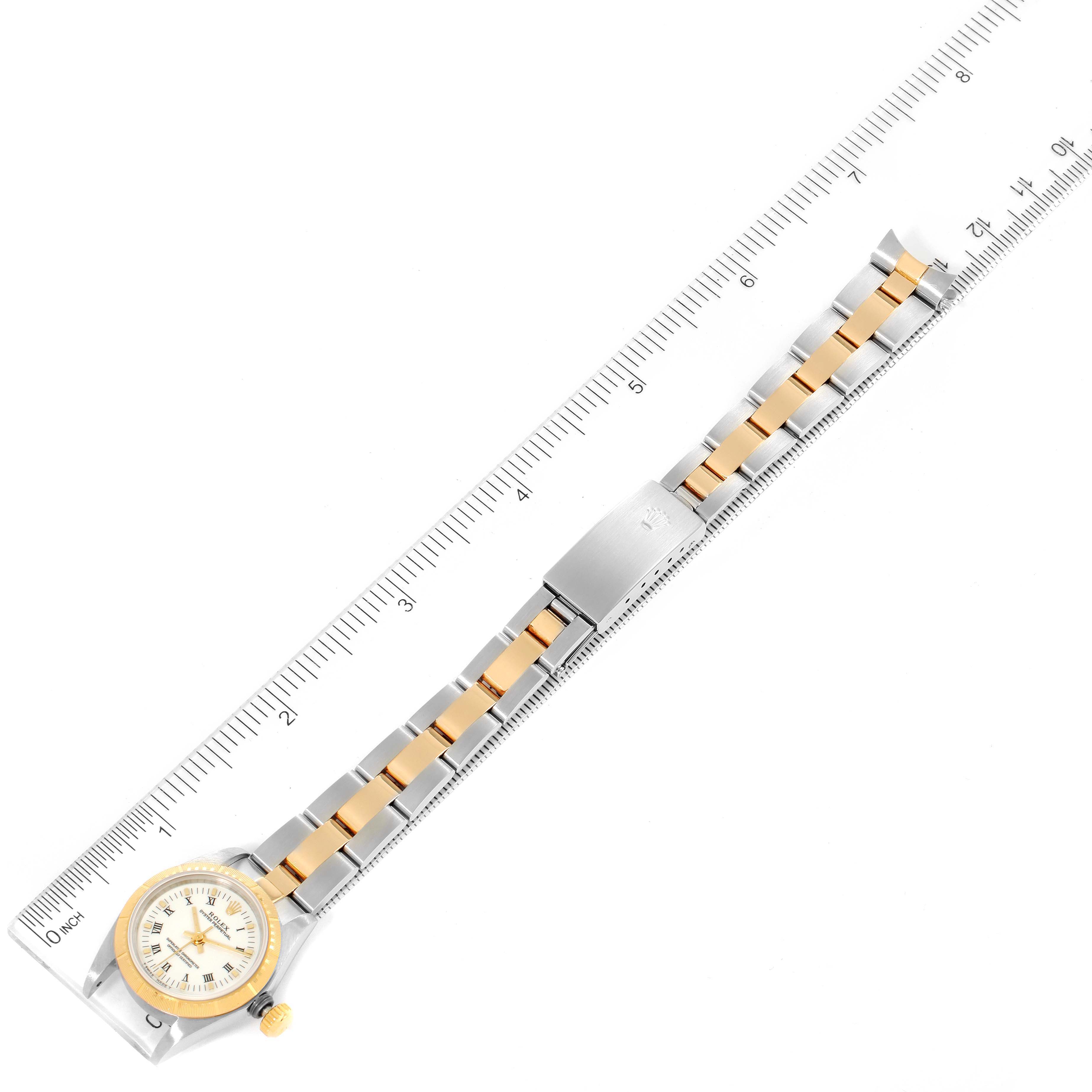 This image shows a top-down view of a Rolex Oyster Perpetual 67243 Women's Steel and Gold (two tone) White Dial 67243 Women's Steel and Gold (two tone) White Dial watch with its bracelet against a ruler for scale.