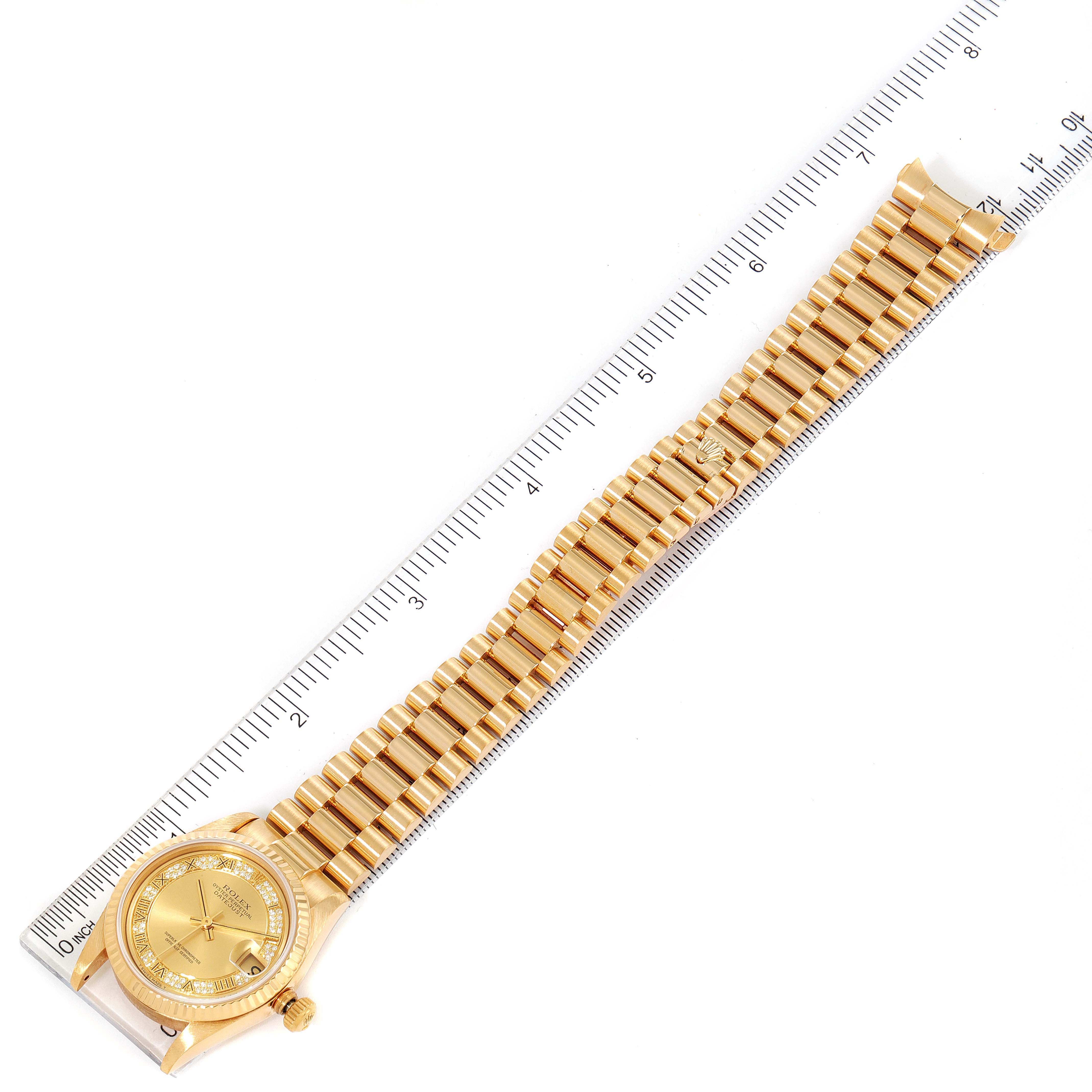 The image shows a top-down view of a Rolex President 68278 Women
s Yellow Gold Champagne Dial 68278 Women
s Yellow Gold Champagne Dial model watch with its full bracelet and a measuring ruler.