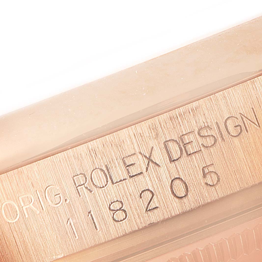 This close-up image of a Rolex President 118205 Men's Rose Gold Silver Dial 118205 Men's Rose Gold Silver Dial watch shows part of its case with the engraved design number "118205".