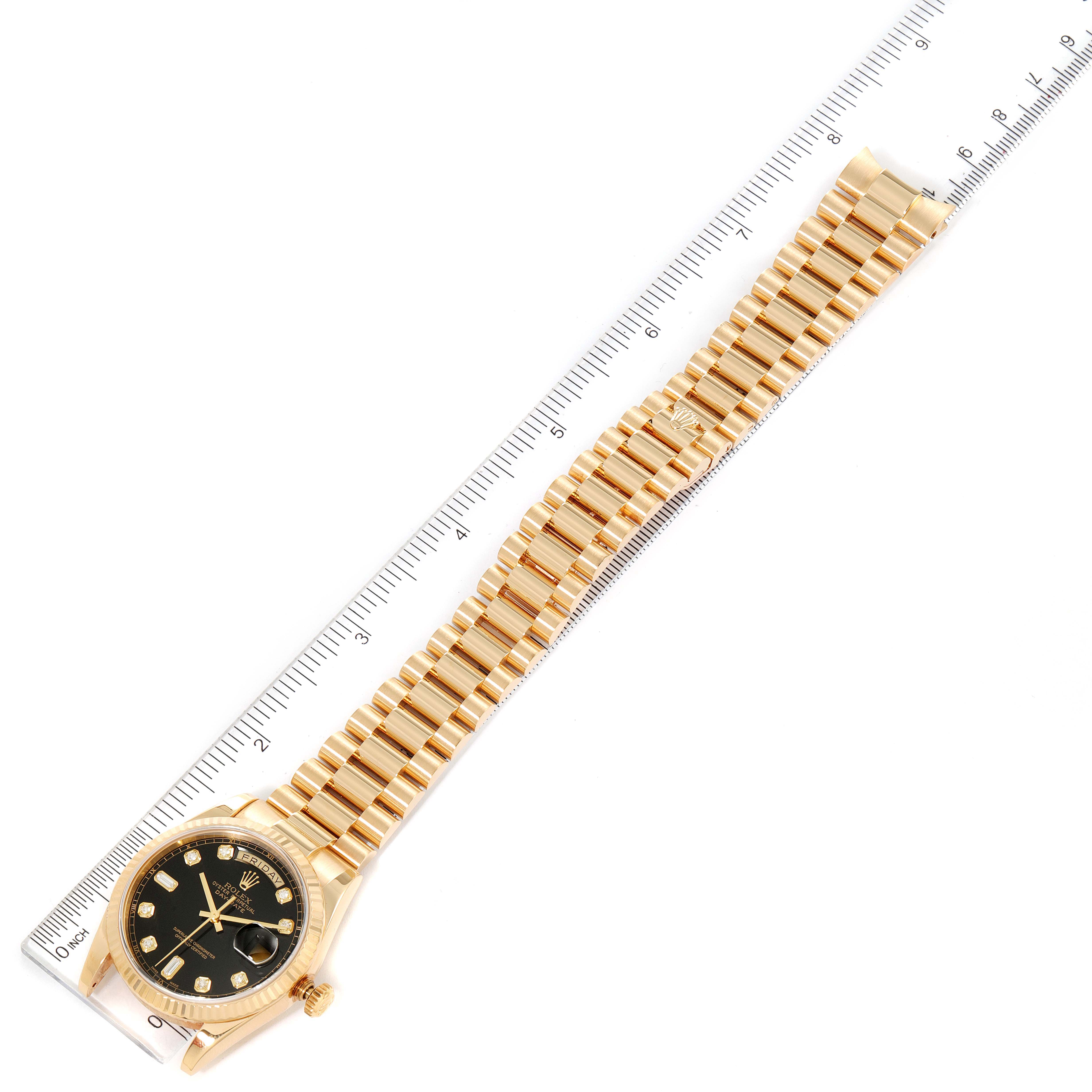 The Rolex President 118238 Men
s Yellow Gold Black Dial 118238 Men
s Yellow Gold Black Dial model watch is shown at a top-down angle, displaying the dial, bezel, bracelet, and part of a ruler for size reference.