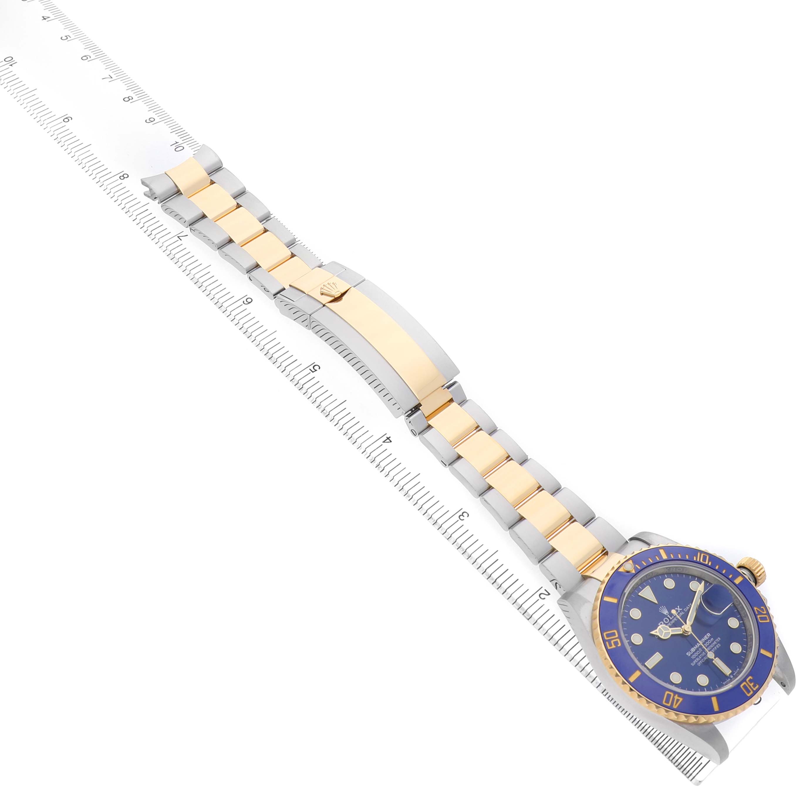 The Rolex Submariner 126613LB Men's Steel and Gold (two tone) Blue Dial watch is shown at an angled view, displaying the blue dial, bezel, and two-tone bracelet alongside a ruler.
