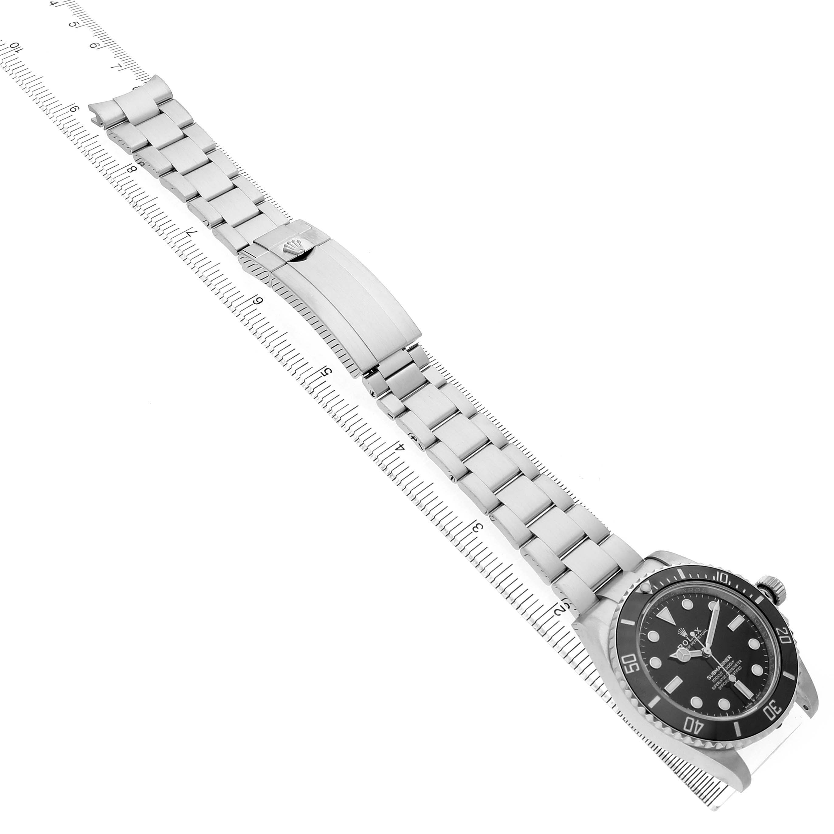 The Rolex Submariner 124060 Men's Stainless Steel Black Dial watch is shown at an angled view, displaying the dial, bezel, bracelet, and clasp on top of a ruler.