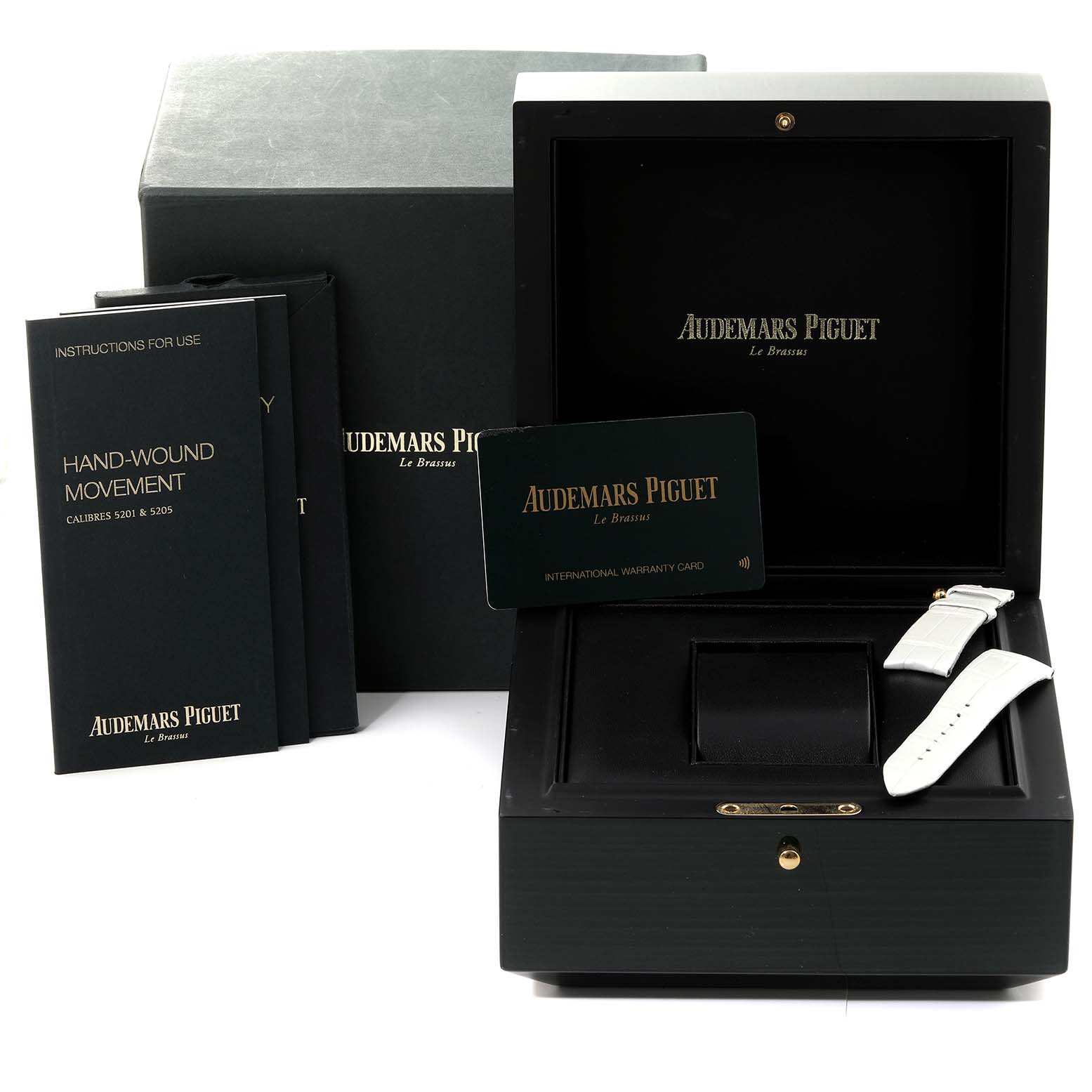 The image shows the box and contents for a Millenary model by Audemars Piguet, including manuals, a warranty card, and a strap.