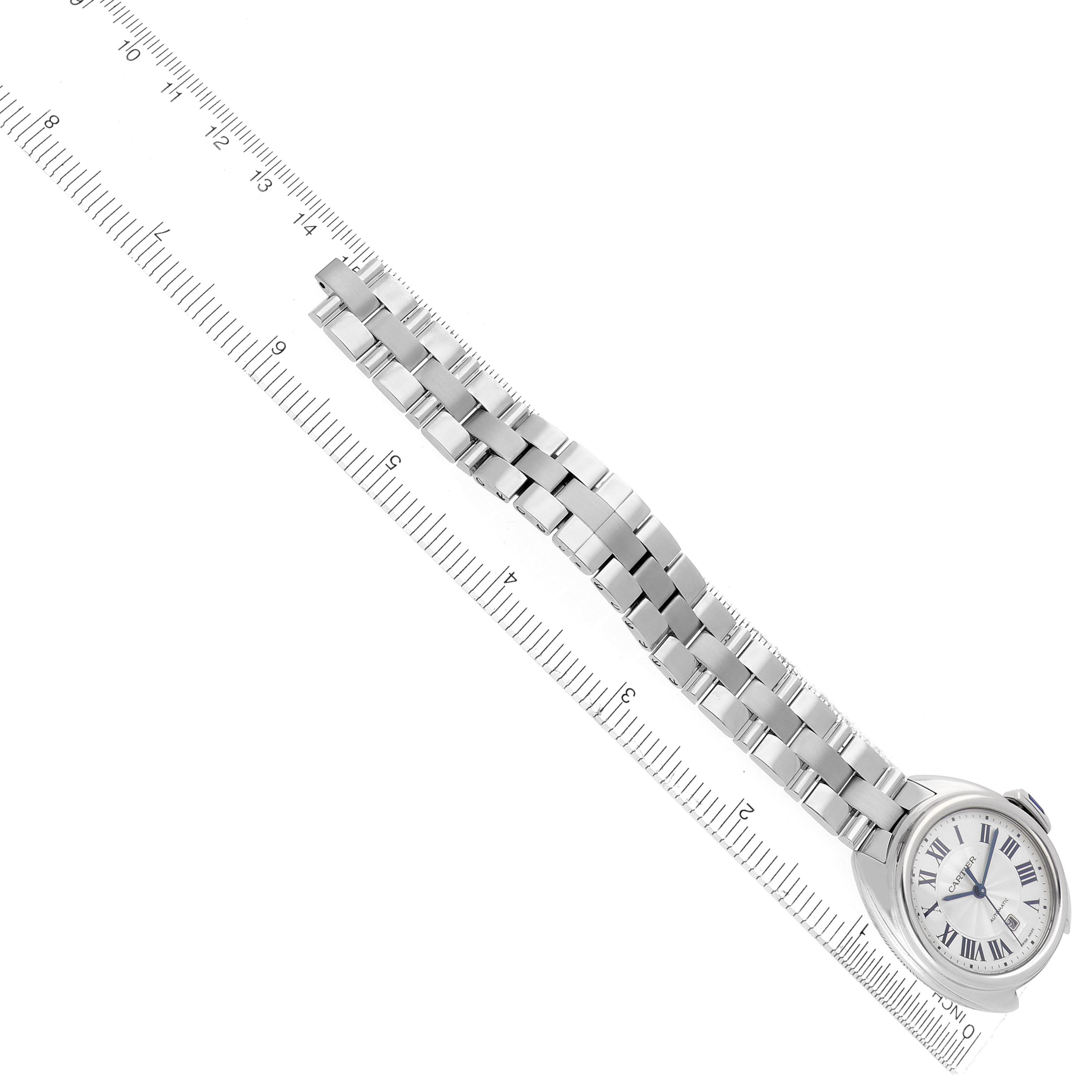 The Cartier Clé watch is shown diagonally with its bracelet and face visible, positioned alongside a ruler.