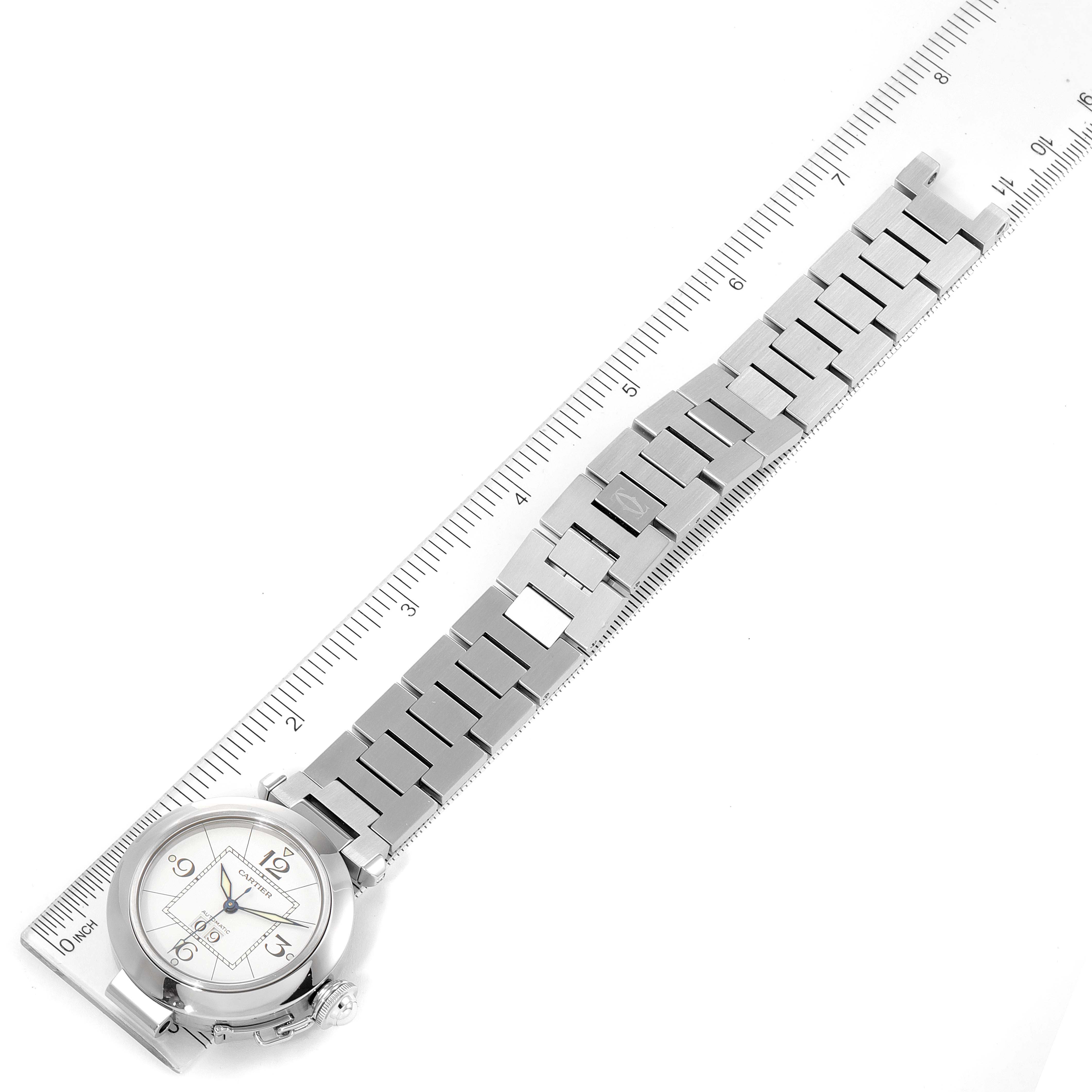 The Cartier Pasha W31055M7 Women's Stainless Steel White Dial W31055M7 Women's Stainless Steel White Dial watch is shown from a top-down angle with its face and metal bracelet visible, alongside a ruler for scale.