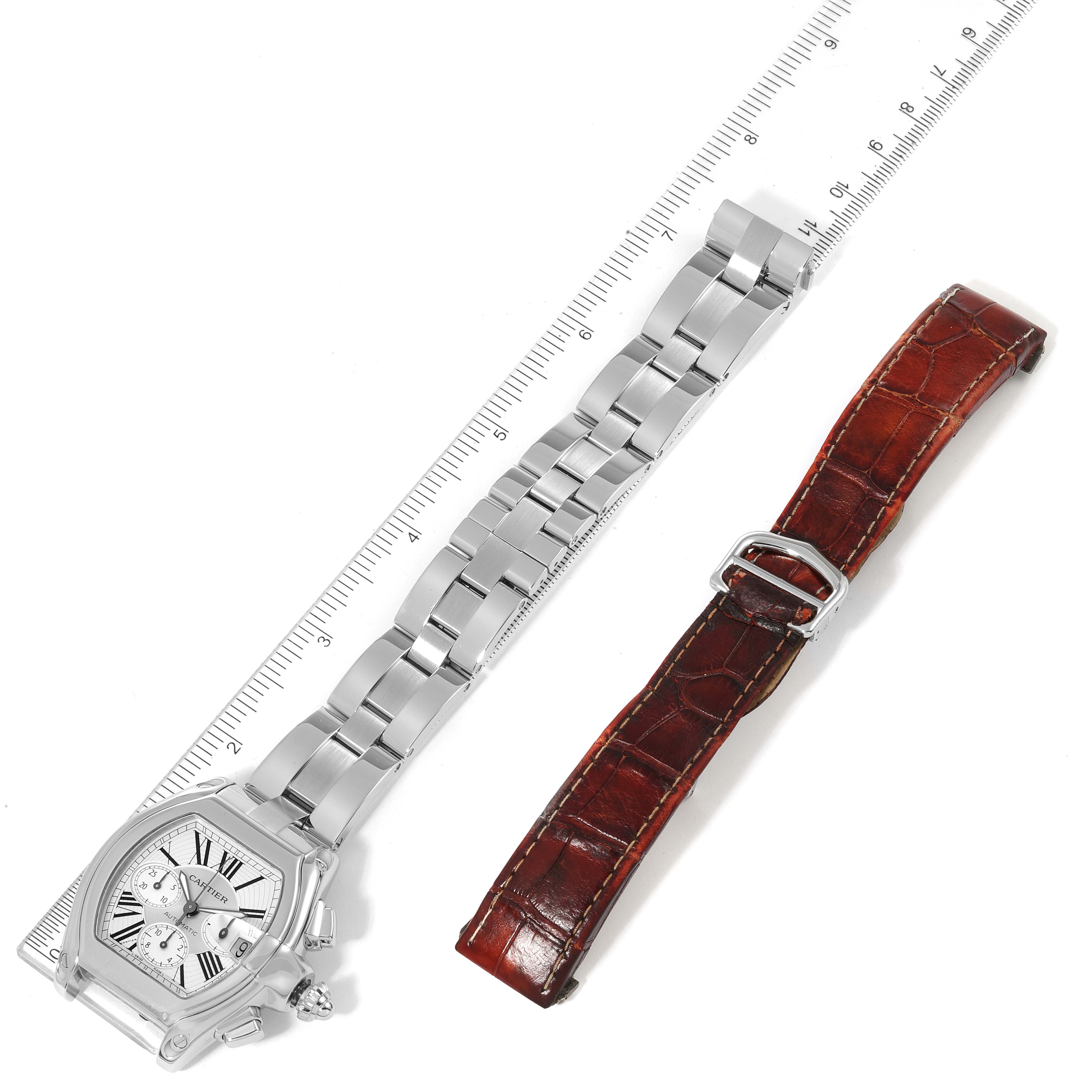 This image shows the Cartier Roadster W62019X6 Men
s Stainless Steel Silver Dial W62019X6 Men
s Stainless Steel Silver Dial watch laid flat beside a brown leather replacement strap on a white background with a ruler for scale.