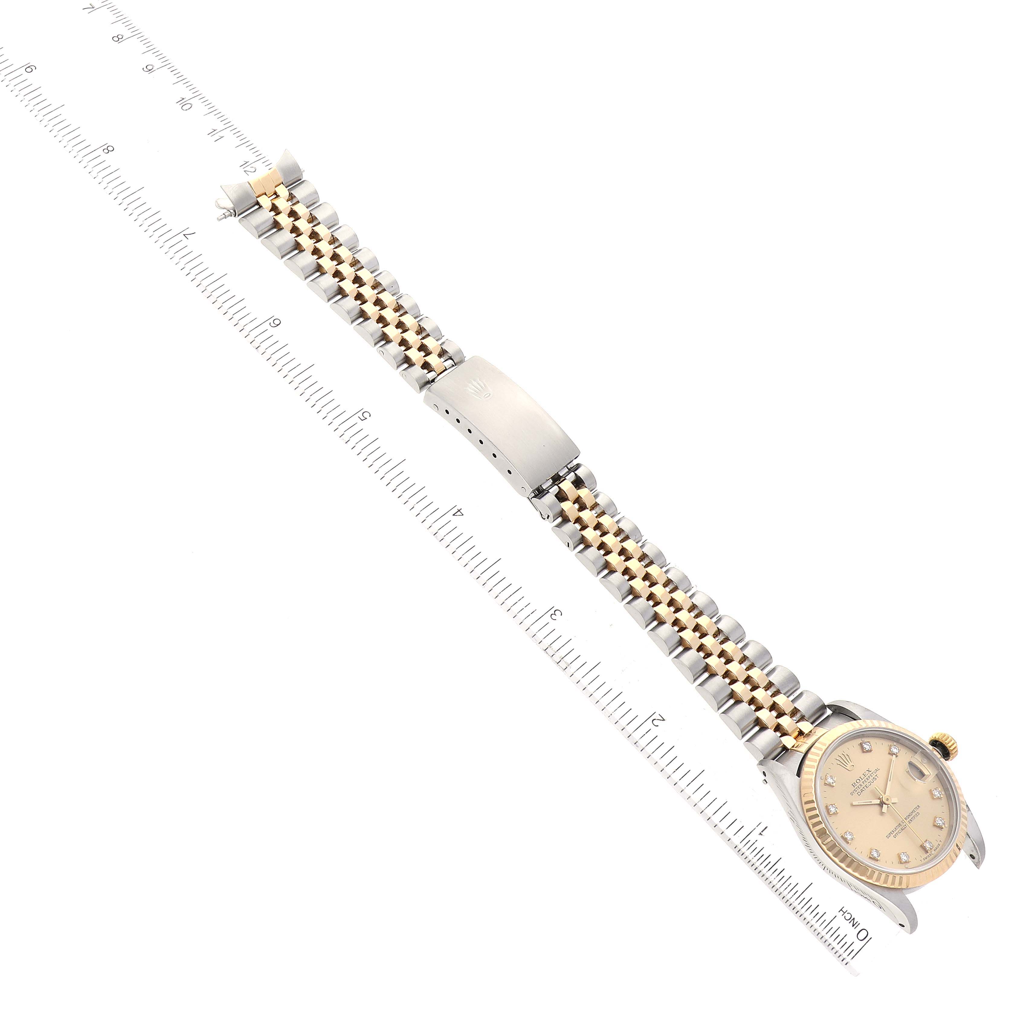 This image shows a top-down view of a Rolex Mid-Size 68273 Women's Steel and Gold (two tone) Champagne Dial 68273 Women's Steel and Gold (two tone) Champagne Dial watch including its band, clasp, and face beside a ruler for scale.