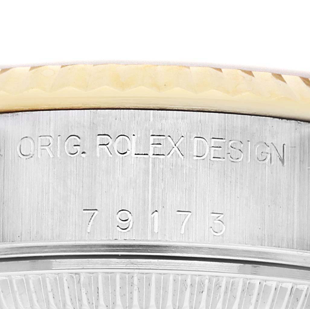 The image shows the side of a Rolex Datejust 79173 Women
s Steel and Gold (two tone) Champagne Dial 79173 Women
s Steel and Gold (two tone) Champagne Dial watch, highlighting the bezel and engraved case with "ORIG. ROLEX DESIGN" and numbers.