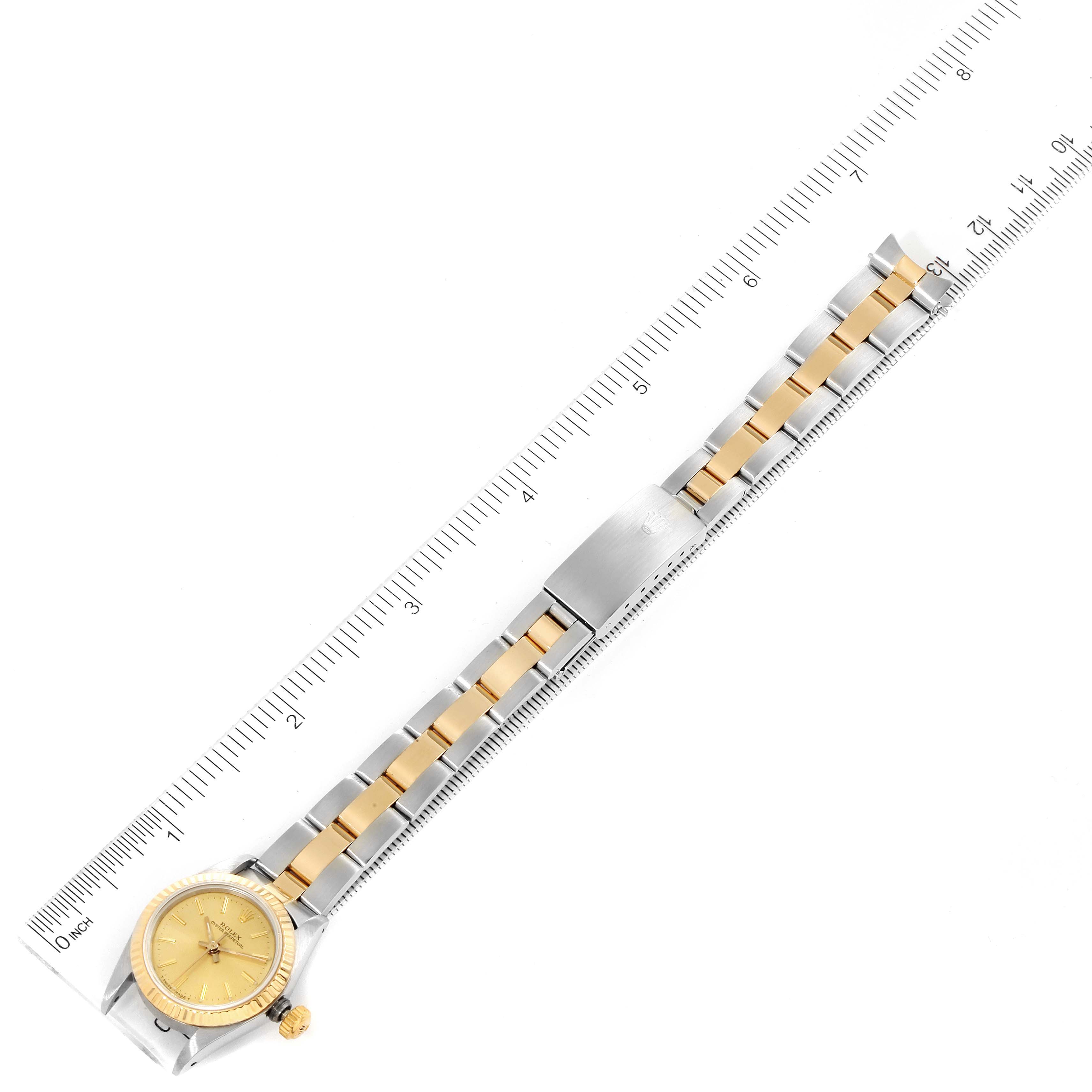 The image shows a Rolex Oyster Perpetual 67193 Women
s Steel and Gold (two tone) Champagne Dial 67193 Women
s Steel and Gold (two tone) Champagne Dial watch laid flat, highlighting the watchband and face beside a ruler for scale.