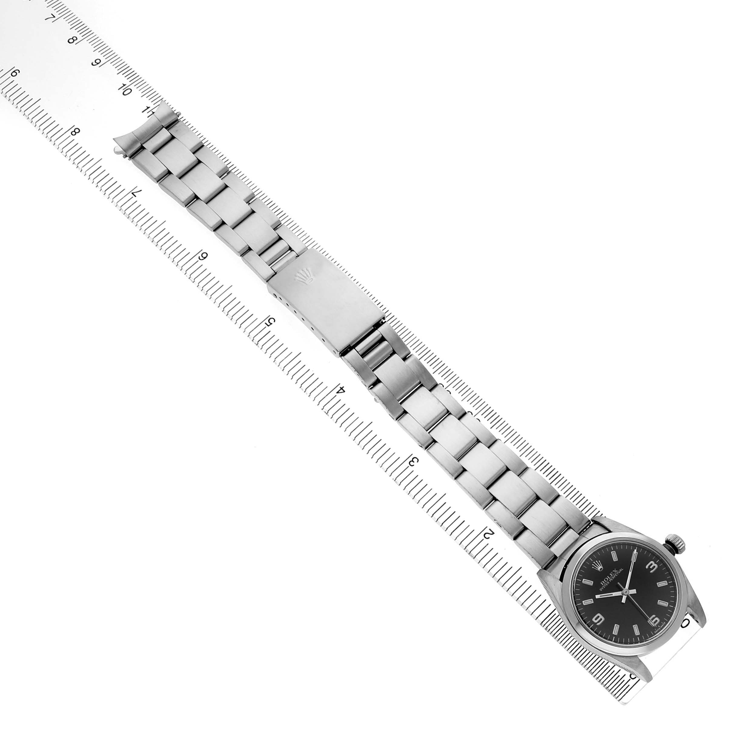 The Rolex Mid-Size 77080 Womens Stainless Steel Black Dial watch is shown from above, featuring the bracelet, clasp, and case with a ruler for scale.