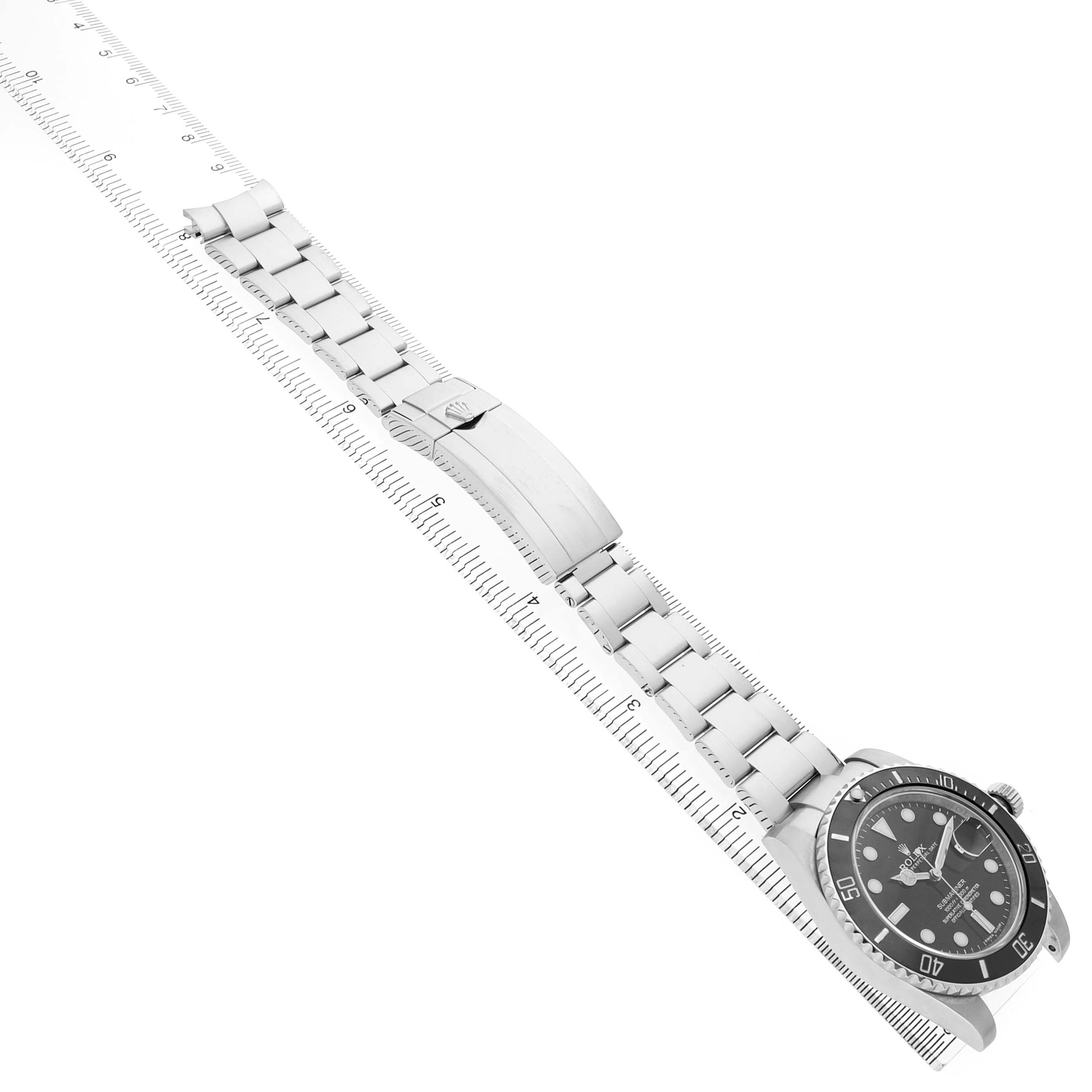 The Rolex Submariner 116610 Mens Stainless Steel Black Dial watch is shown at an angled top view, displaying the face, bezel, and stainless steel bracelet against a ruler.