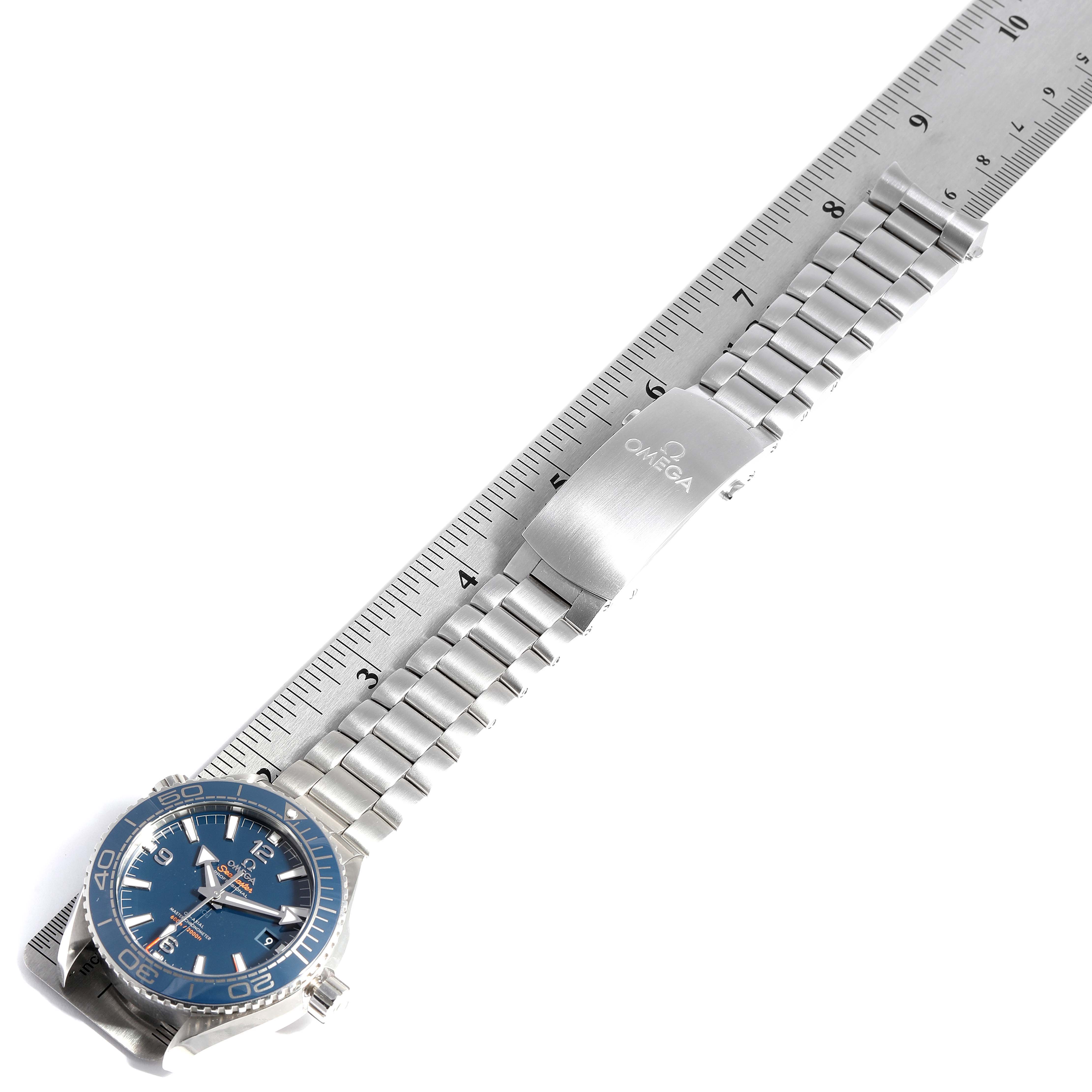The image shows the Omega Planet Ocean 215.30.44.21.03.001  Men
s Stainless Steel Blue Dial 215.30.44.21.03.001  Men
s Stainless Steel Blue Dial watch laid flat with its metal bracelet extended alongside a ruler.