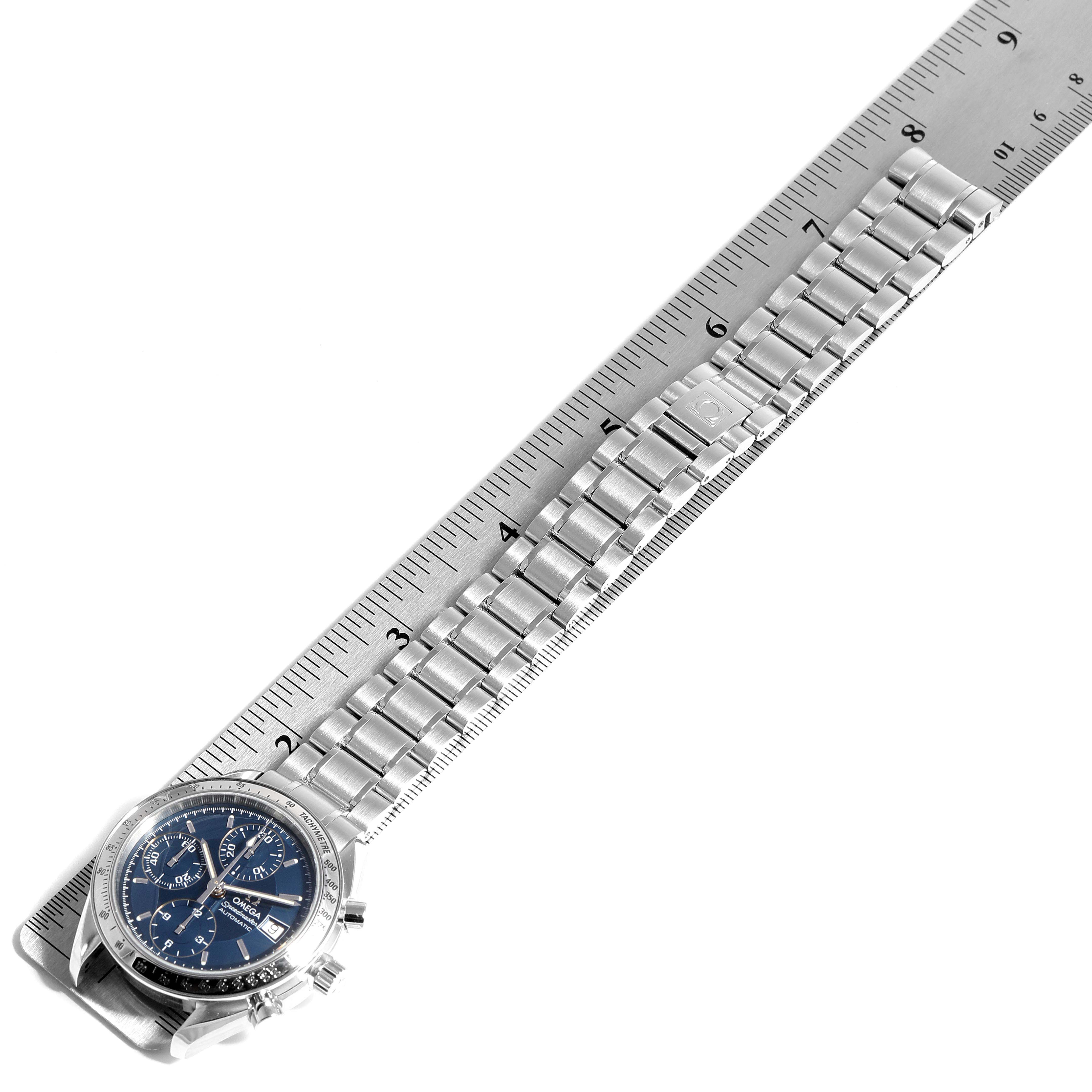 The image displays an Omega Speedmaster 3511.80.00 Men
s Stainless Steel Blue Dial 3511.80.00 Men
s Stainless Steel Blue Dial watch positioned next to a ruler, showing the watch face and metallic bracelet.