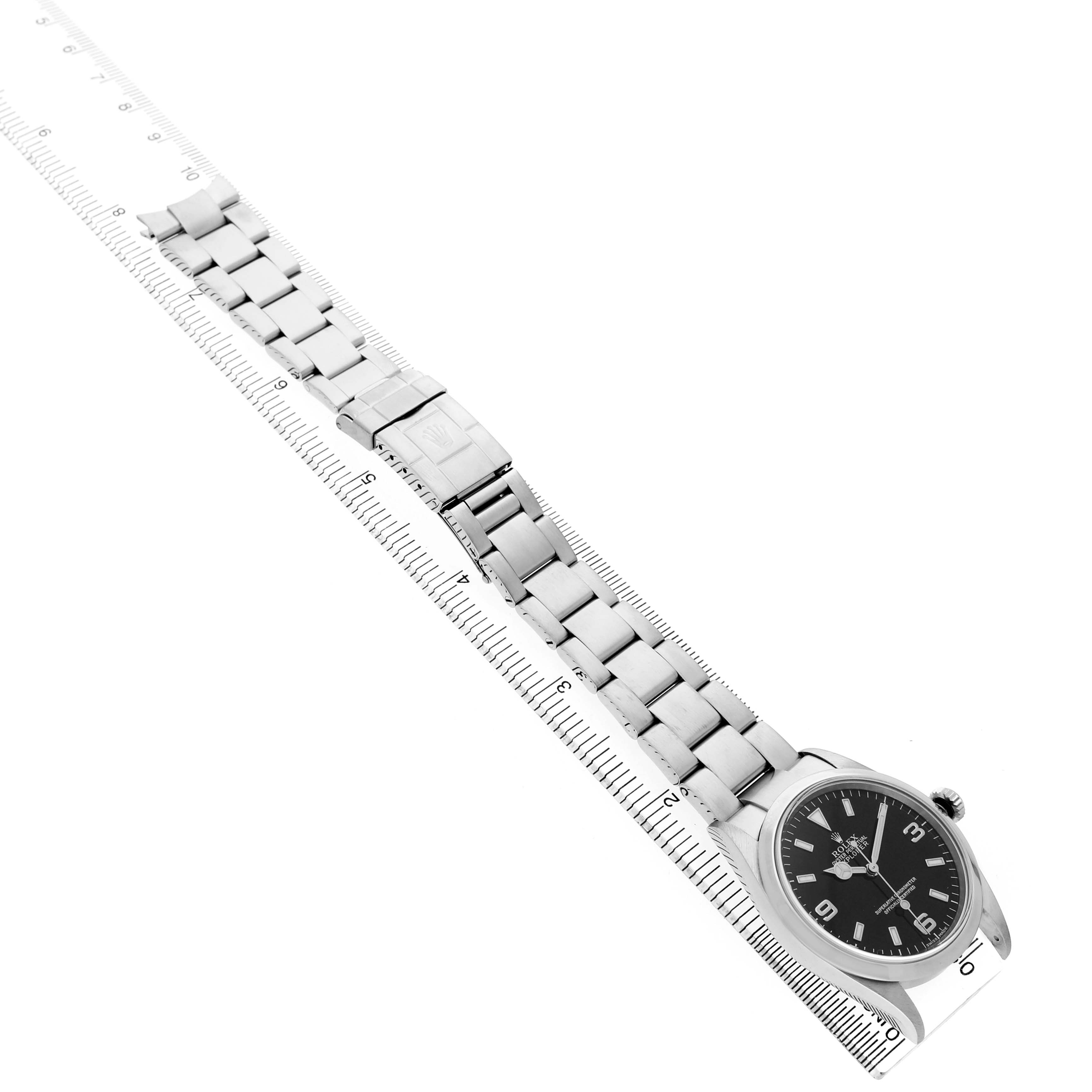 The Rolex Explorer 114270 Men's Stainless Steel Black Dial watch is shown diagonally with its face, bracelet, and clasp visible, alongside a measuring ruler.