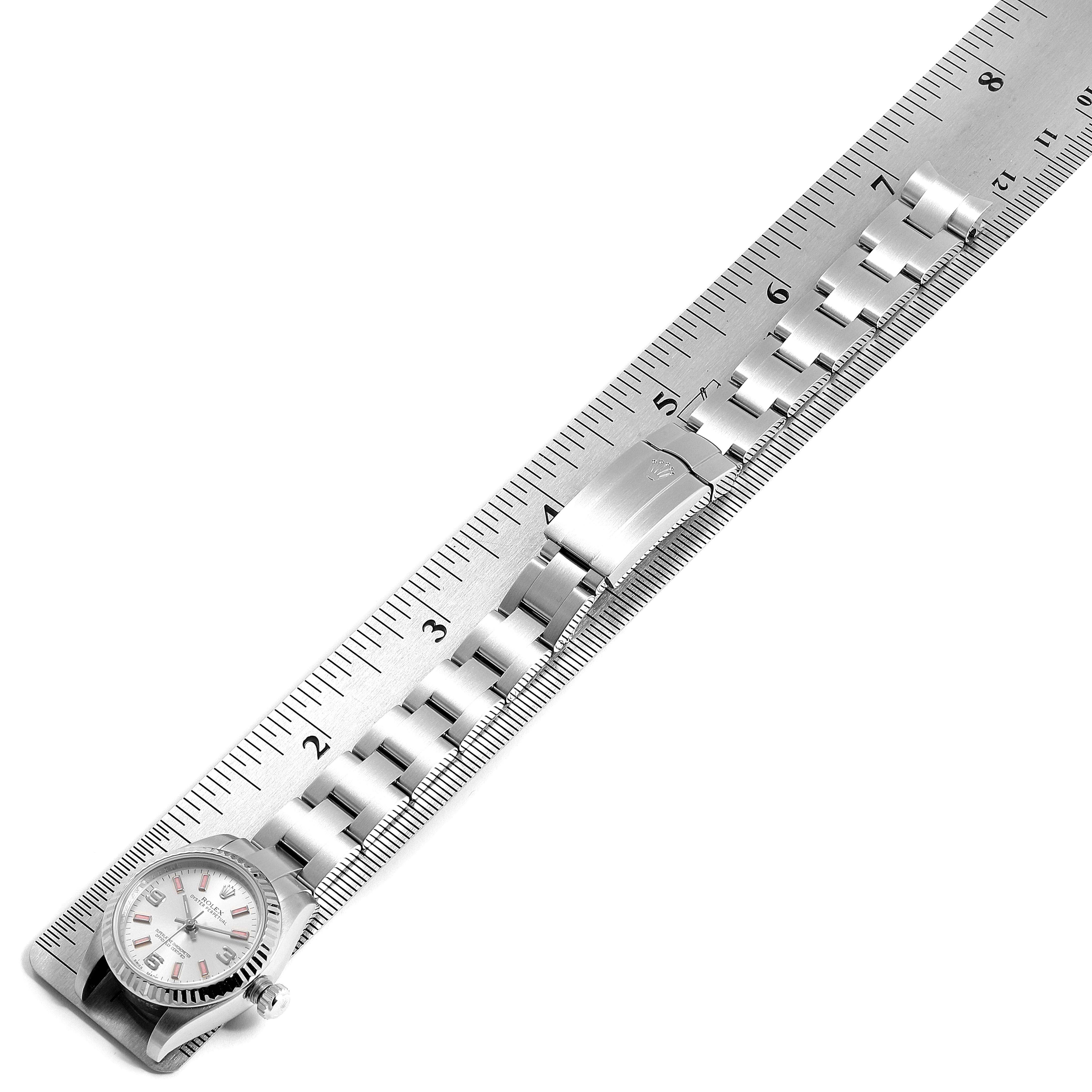 The Oyster Perpetual Rolex watch is shown from a top-down angle with the face and bracelet visible, alongside a ruler.