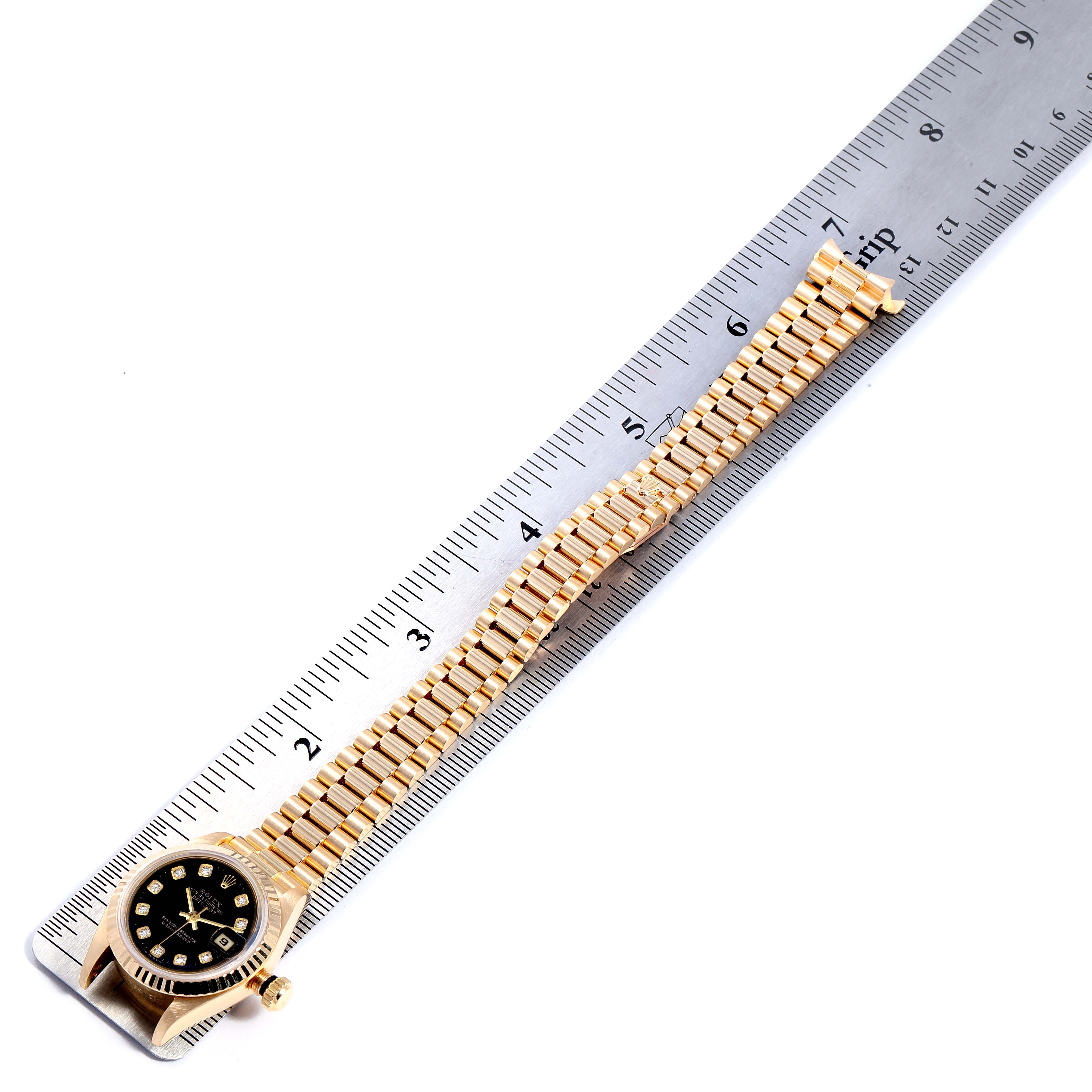 The image shows a Rolex President 69178 Women's Yellow Gold Black Dial 69178 Women's Yellow Gold Black Dial model watch laid flat next to a ruler, highlighting the watch face and bracelet in a top-down view.
