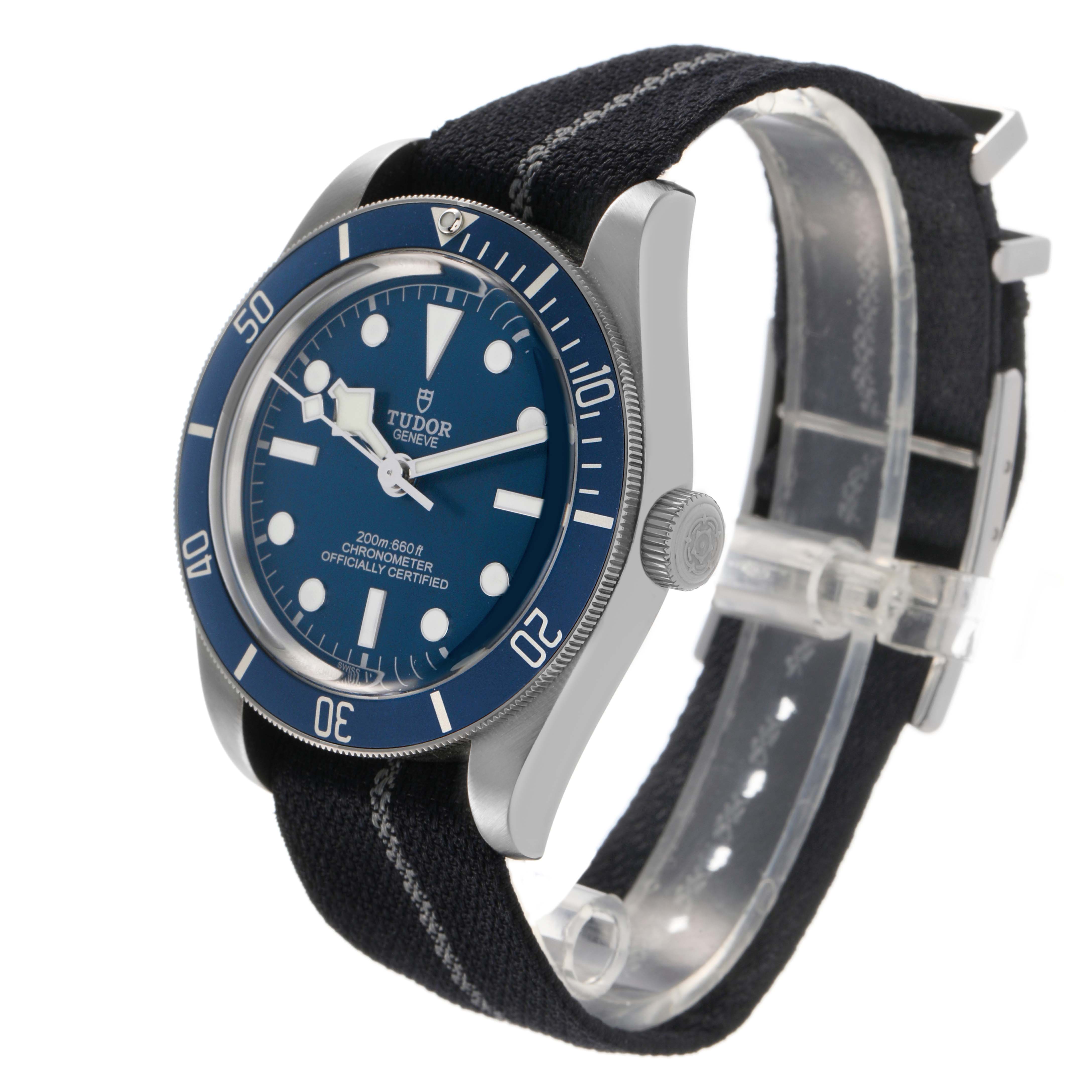 The Tudor Heritage Black Bay 79030 Men's Stainless Steel Brown Dial watch is shown at a three-quarter angle, displaying the dial, bezel, crown, and fabric strap.