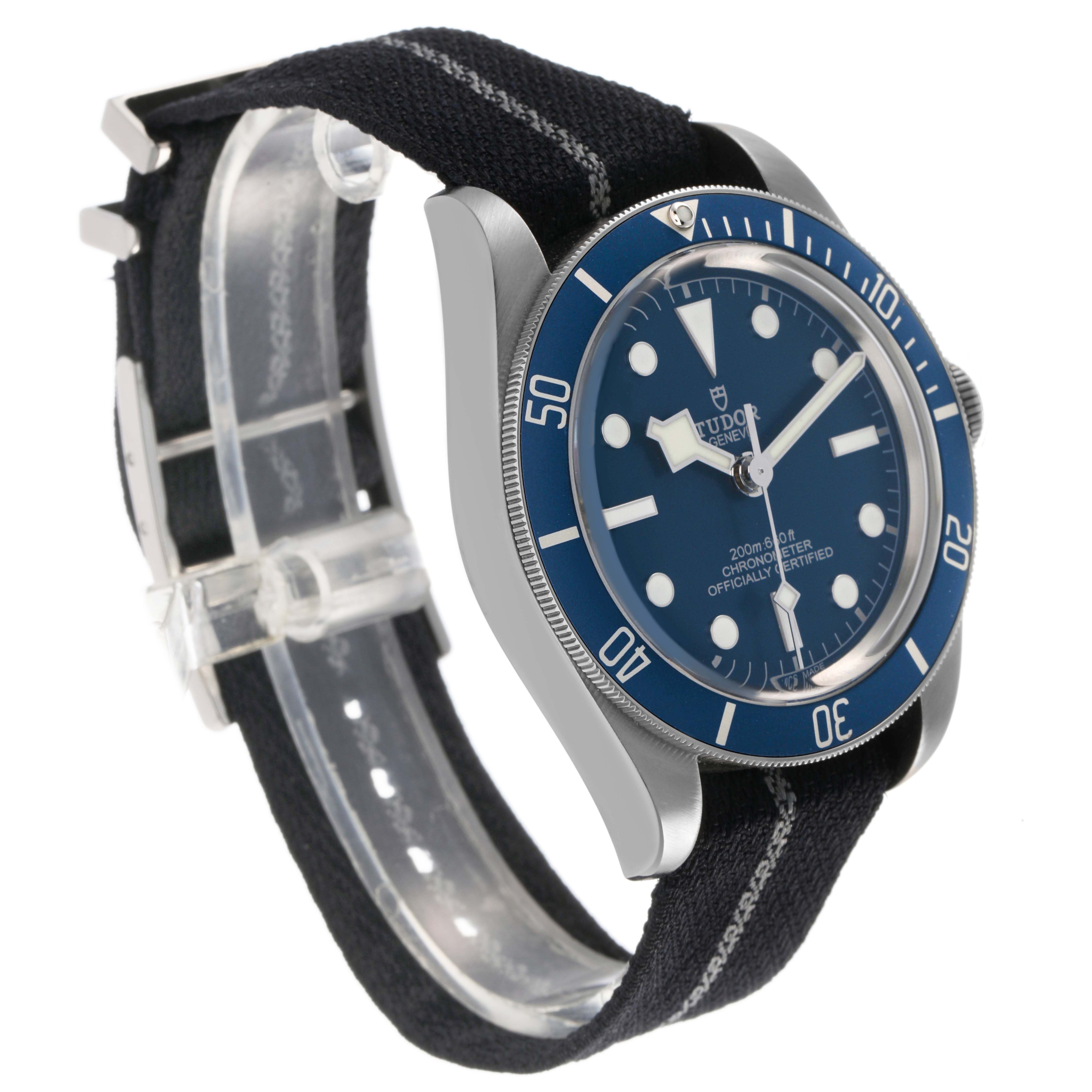 The Tudor Heritage Black Bay 79030 Men's Stainless Steel Brown Dial watch is shown at a three-quarter angle, displaying the bezel, face, case, and fabric strap.