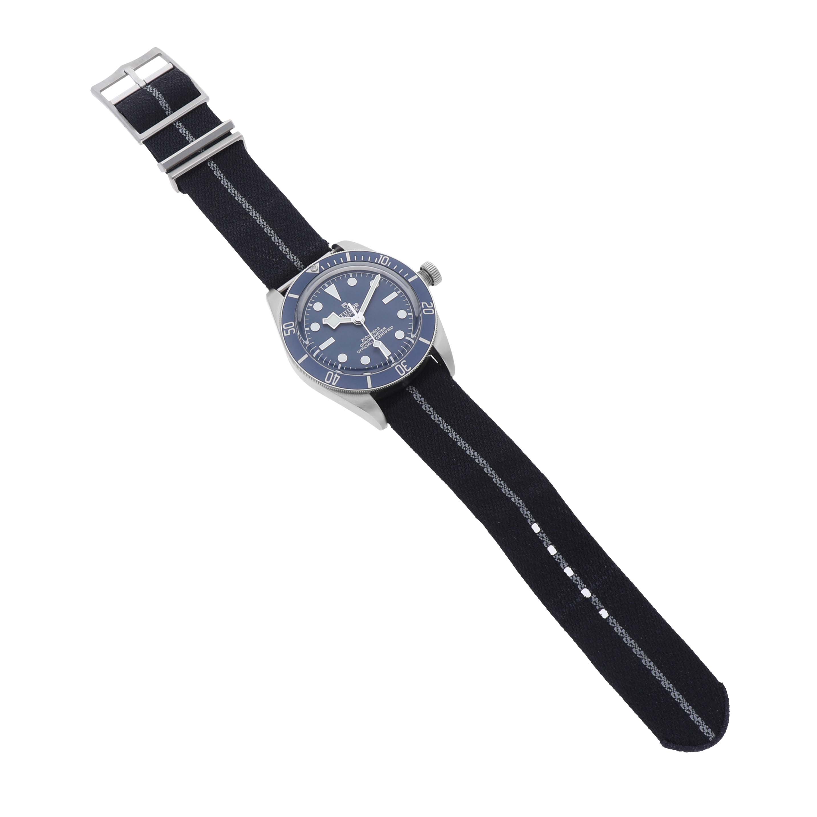 The Tudor Heritage Black Bay 79030 Men's Stainless Steel Brown Dial watch is shown from a slightly angled top view, highlighting its dial, bezel, and fabric strap.