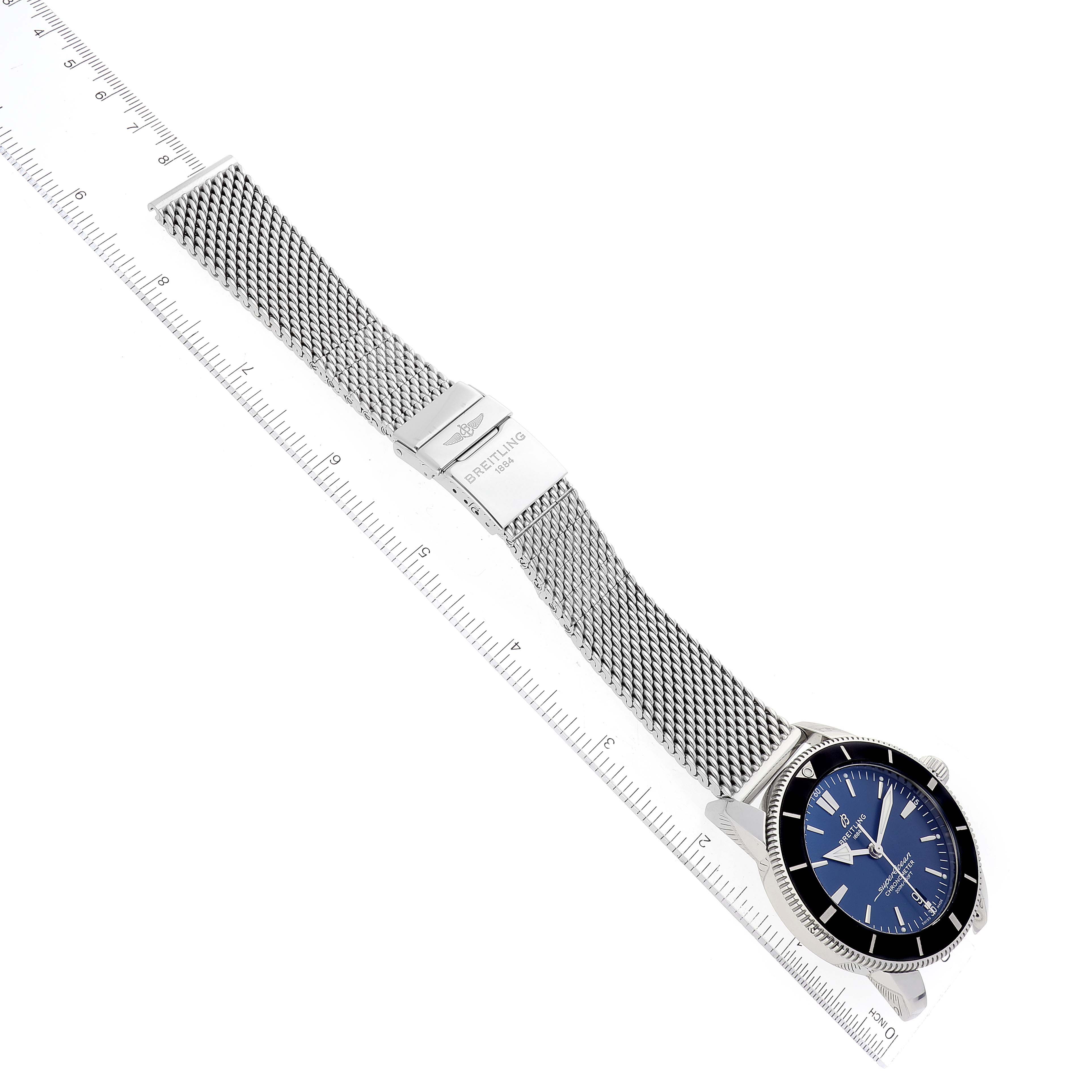 The image shows a Breitling Superocean AB2030 Men's Stainless Steel Blue Dial AB2030 Men's Stainless Steel Blue Dial watch laid flat, with a focus on its mesh bracelet, clasp, and blue dial with an accompanying ruler for scale.