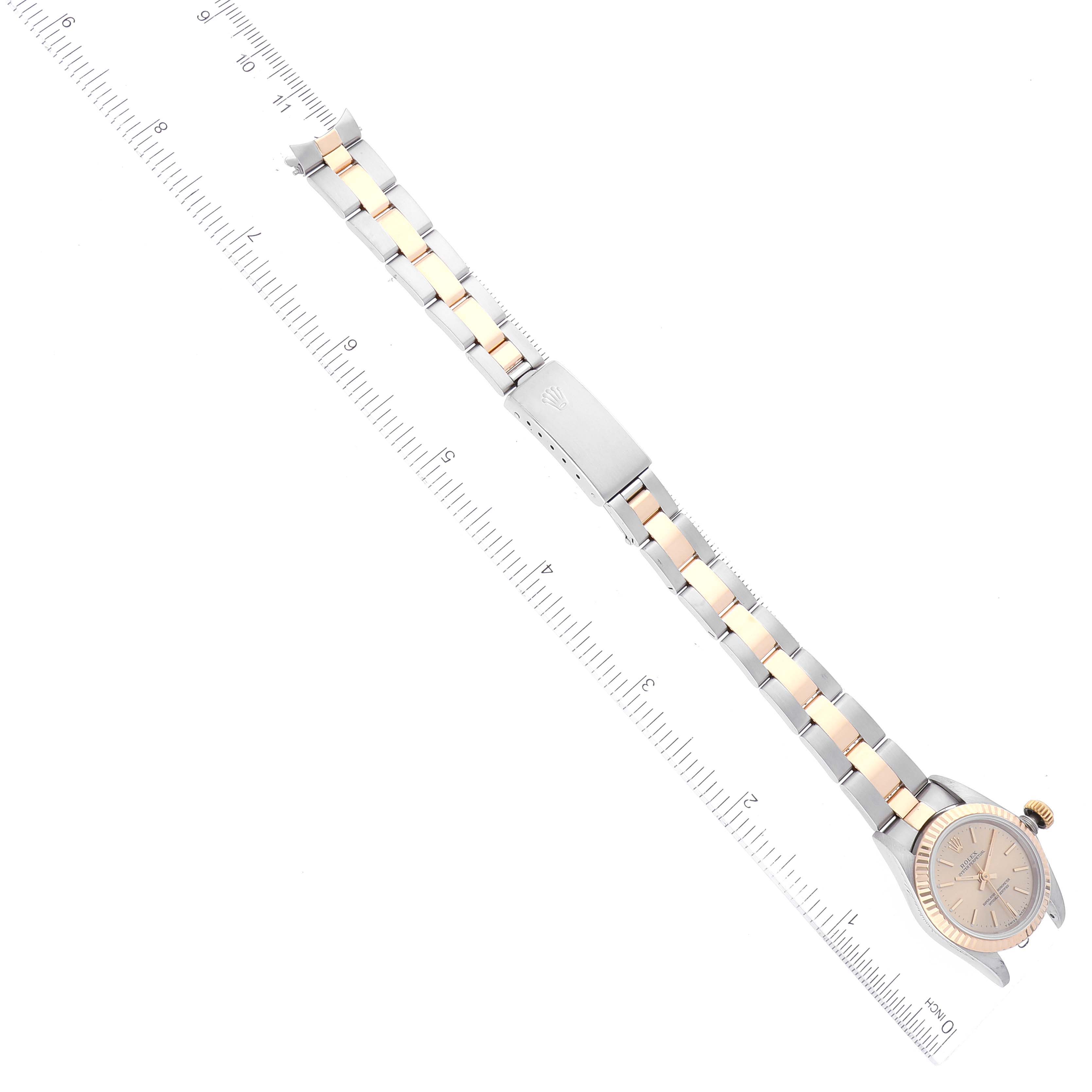 The image shows an overhead view of a Rolex Oyster Perpetual 67193 Women's Steel and Gold (two tone) Champagne Dial 67193 Women's Steel and Gold (two tone) Champagne Dial watch with a two-tone bracelet laid next to a ruler.