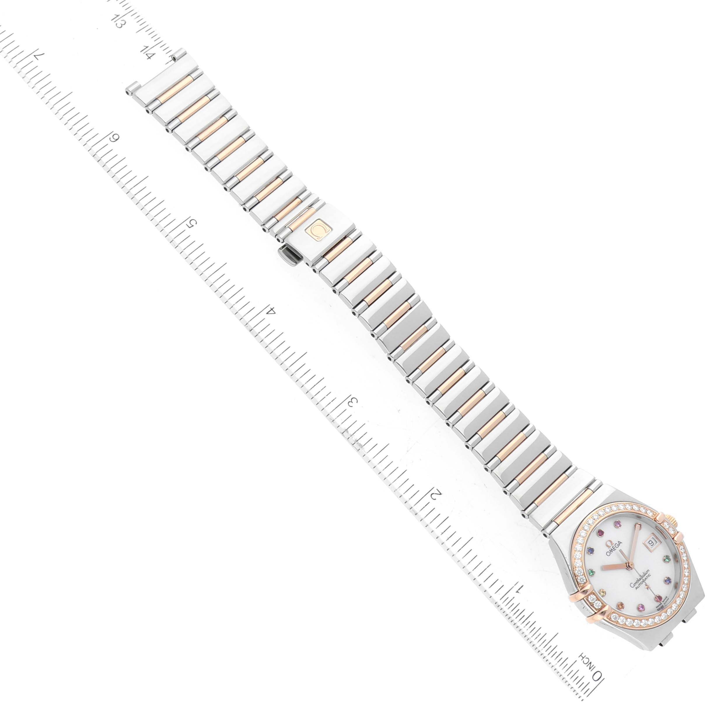 The image shows an Omega 1394.79.00 Women's Steel and Gold (two tone) Mother of Pearl Dial 1394.79.00 Women's Steel and Gold (two tone) Mother of Pearl Dial Constellation Iris Rainbow Steel Rose Gold Multi Stone Ladies Watch 1394.79.00 laid flat with its band extended alongside a ruler.