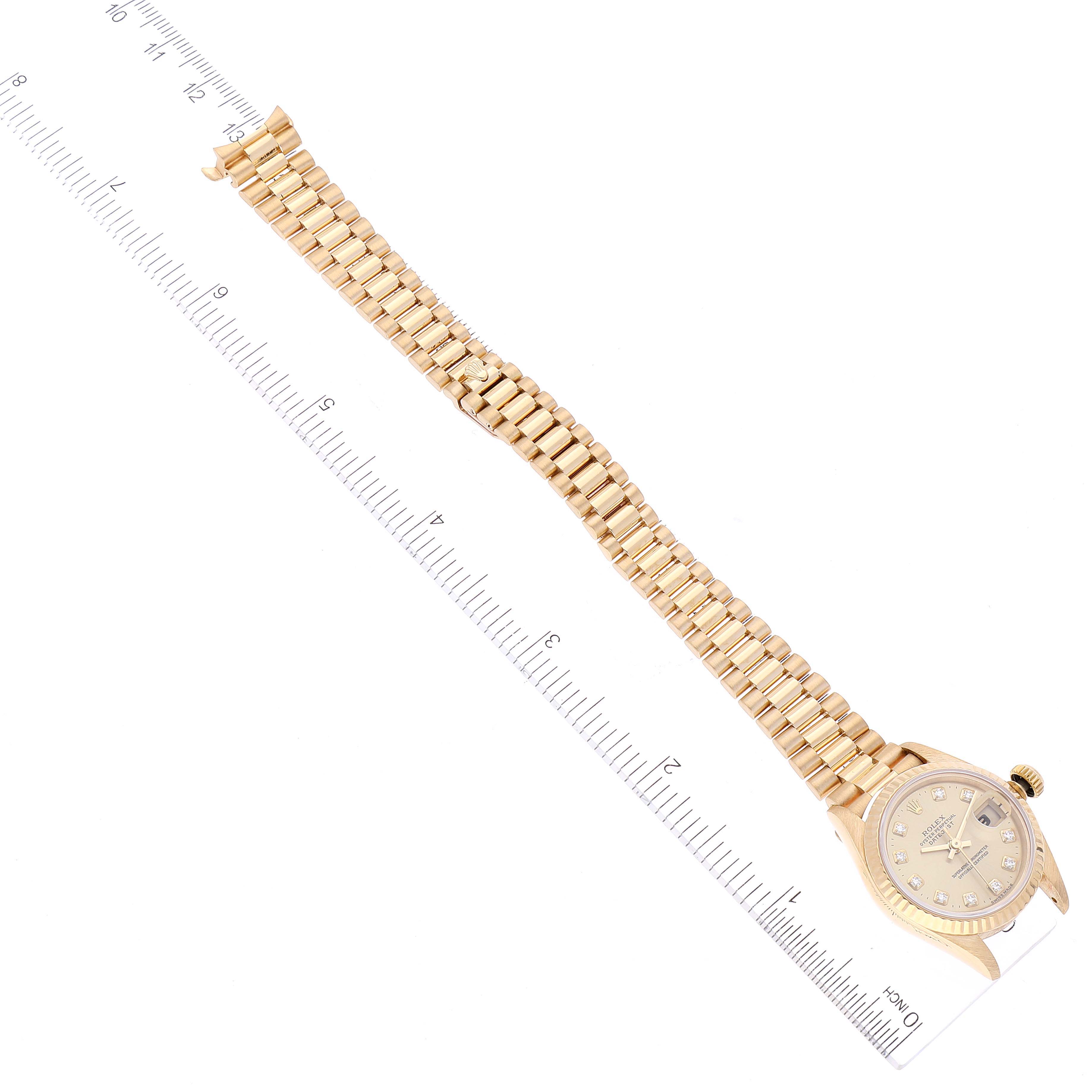 The image shows a Rolex President 69178 Women
s Yellow Gold Champagne Dial 69178 Women
s Yellow Gold Champagne Dial model watch laid flat, displaying the full bracelet and the dial at an angle, alongside a ruler.