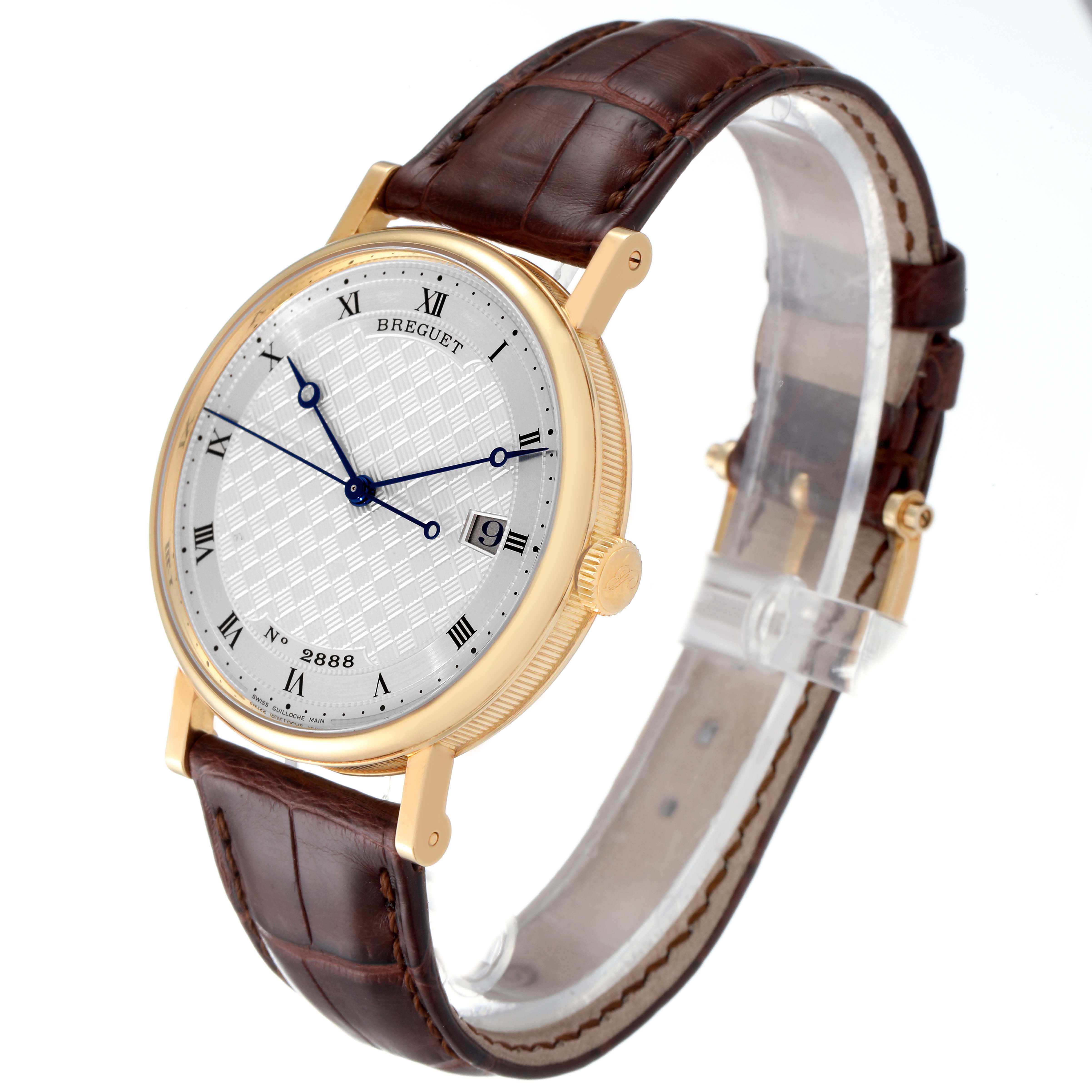 The Breguet Classique 5177BA Men's Yellow Gold Silver Dial 5177BA Men's Yellow Gold Silver Dial watch is shown at a three-quarter angle, highlighting its gold case, dial, and brown leather strap.