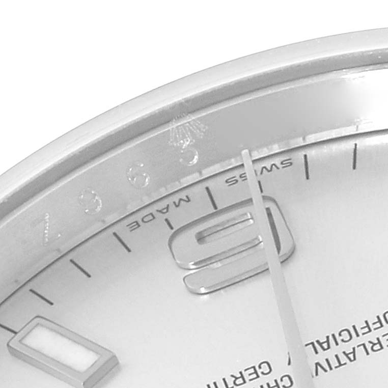 This close-up image of the Rolex Air-King 114210 Men's Stainless Steel Silver Dial 114210 Men's Stainless Steel Silver Dial watch shows part of the dial, hour markers, and hands at an angled view.