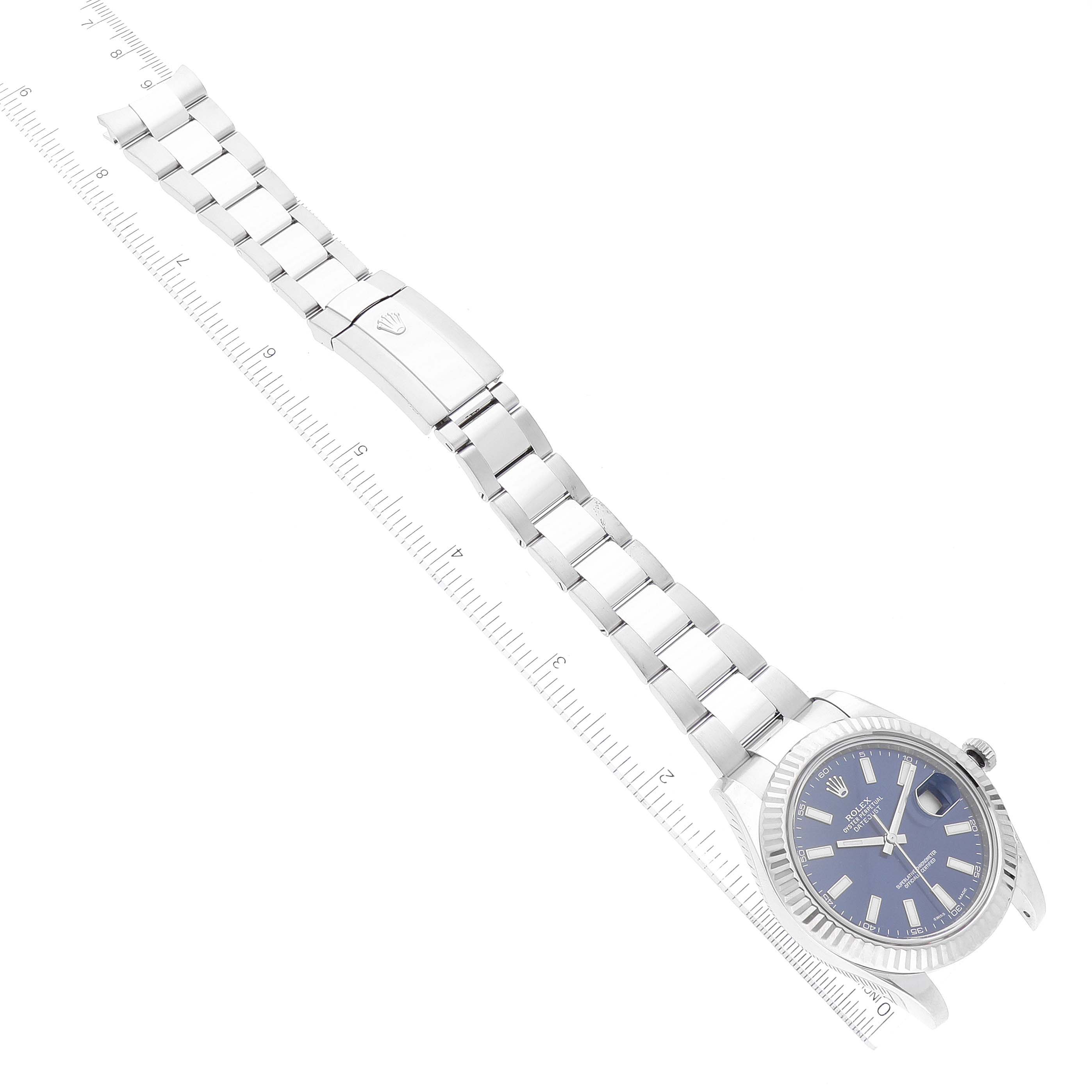 The Rolex Datejust 41 116334 Men
s Stainless Steel Blue Dial 116334 Men
s Stainless Steel Blue Dial watch is shown from an angled top-down view, displaying the bracelet, clasp, and face with a measuring ruler alongside.