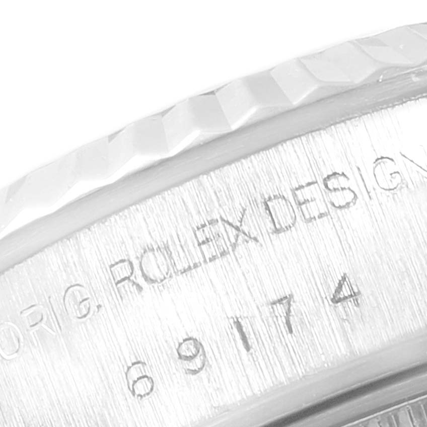 The image shows an angled close-up of the side of the Rolex Datejust 69174 Women
s Stainless Steel Silver Dial 69174 Women
s Stainless Steel Silver Dial
s case, highlighting the fluted bezel and engraved markings.