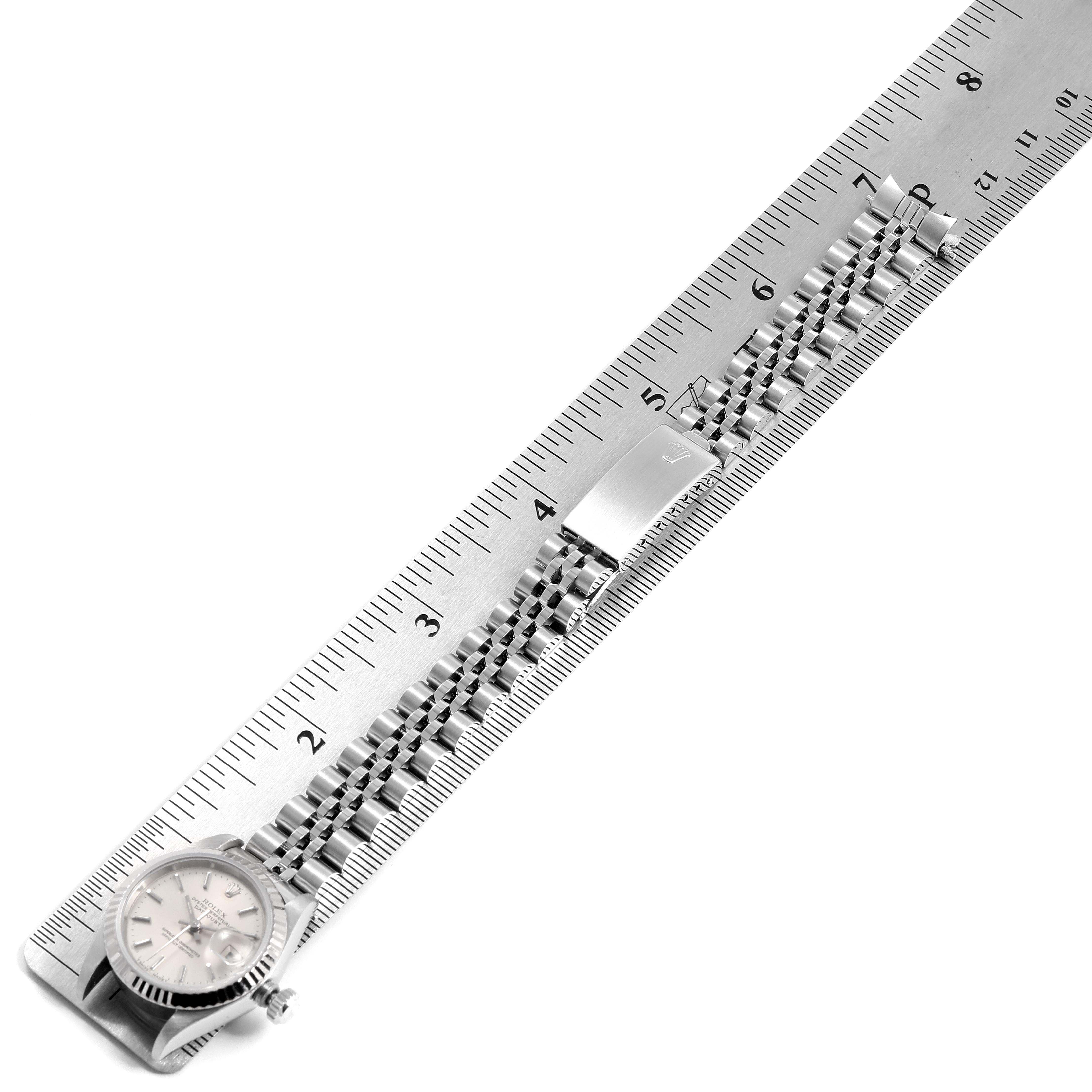 The image shows a Rolex Datejust 69174 Women
s Stainless Steel Silver Dial 69174 Women
s Stainless Steel Silver Dial watch laid flat along a ruler, displaying its face and Jubilee bracelet.