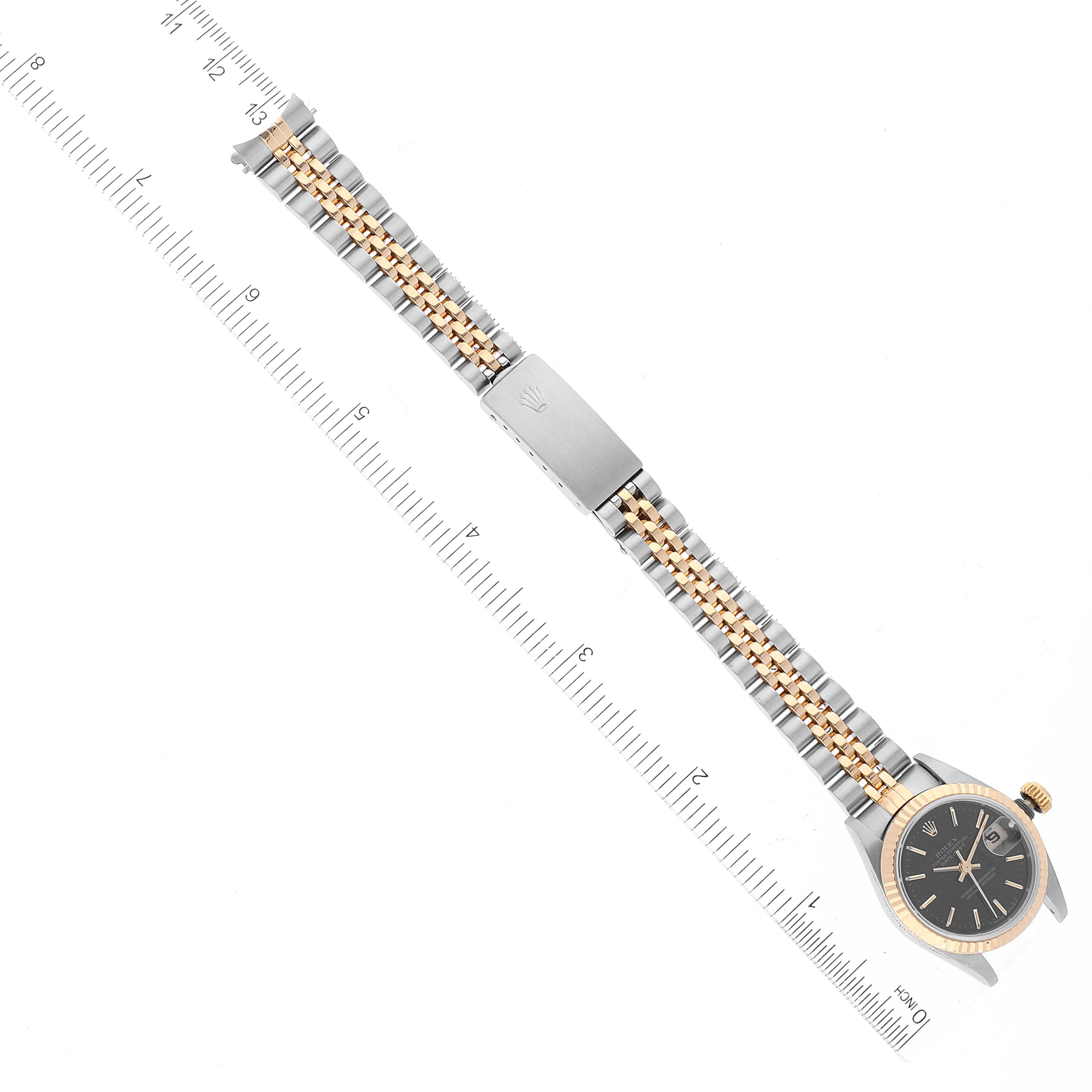 The image shows a Rolex Datejust 69173 Women's Steel and Gold (two tone) Black Dial 69173 Women's Steel and Gold (two tone) Black Dial watch from a top-down angle, displaying the entire face and bracelet against a metric ruler.