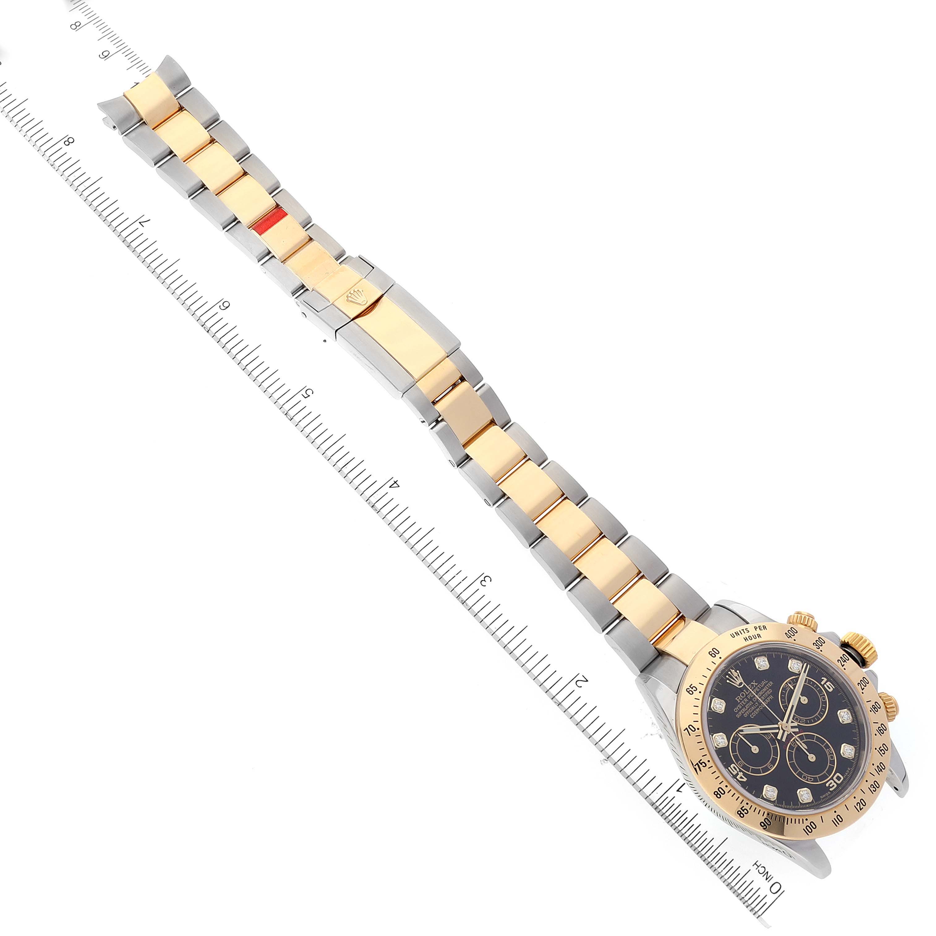 The image displays a Rolex Daytona 116523 Men's Steel and Gold (two tone) Black Dial 116523 Men's Steel and Gold (two tone) Black Dial watch laid flat from an overhead angle, with its full length measured against a ruler.
