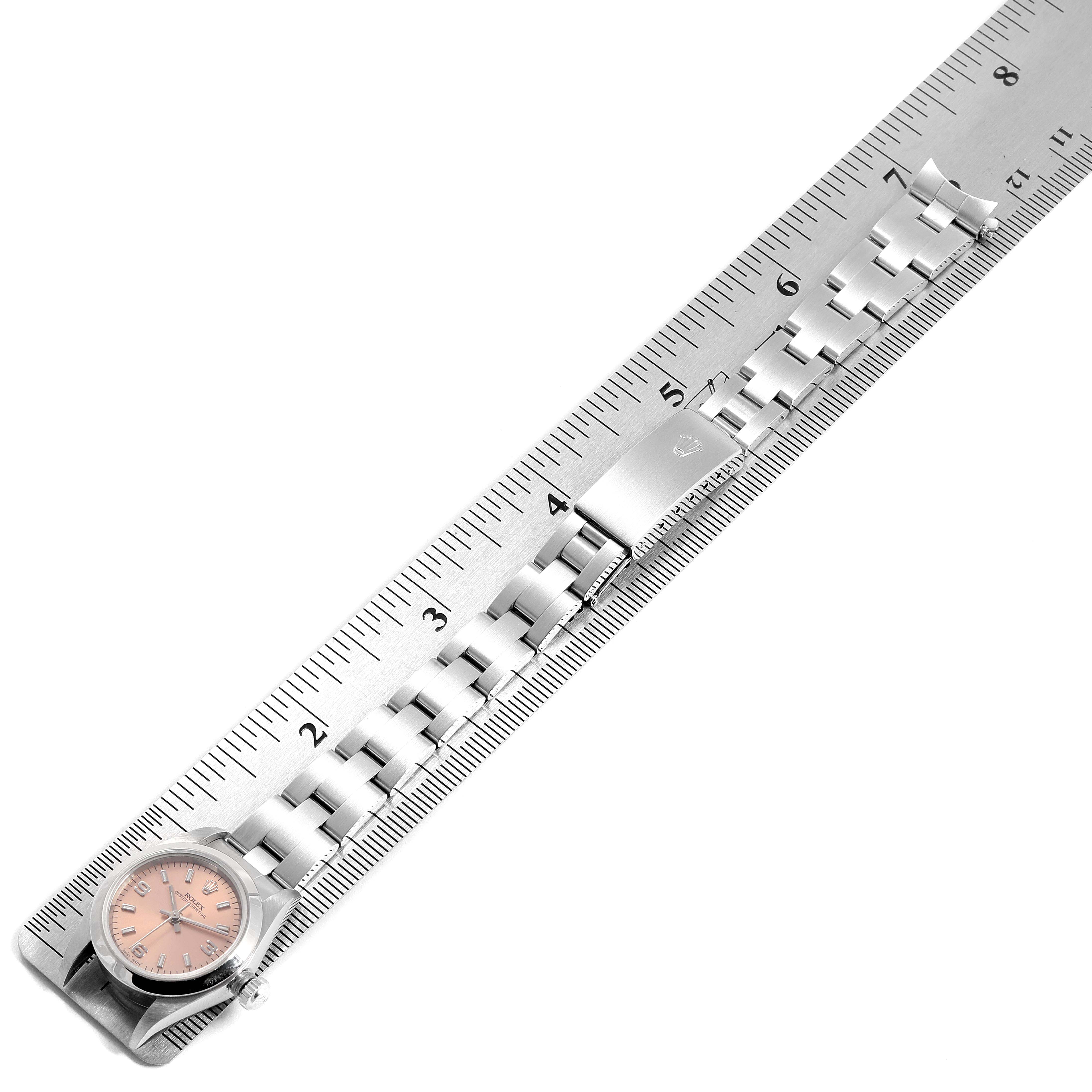 The image shows a top-down view of a Rolex Oyster Perpetual 76080 Women's Stainless Steel Pink Dial 76080 Women's Stainless Steel Pink Dial watch with its metal bracelet laid out along a ruler.