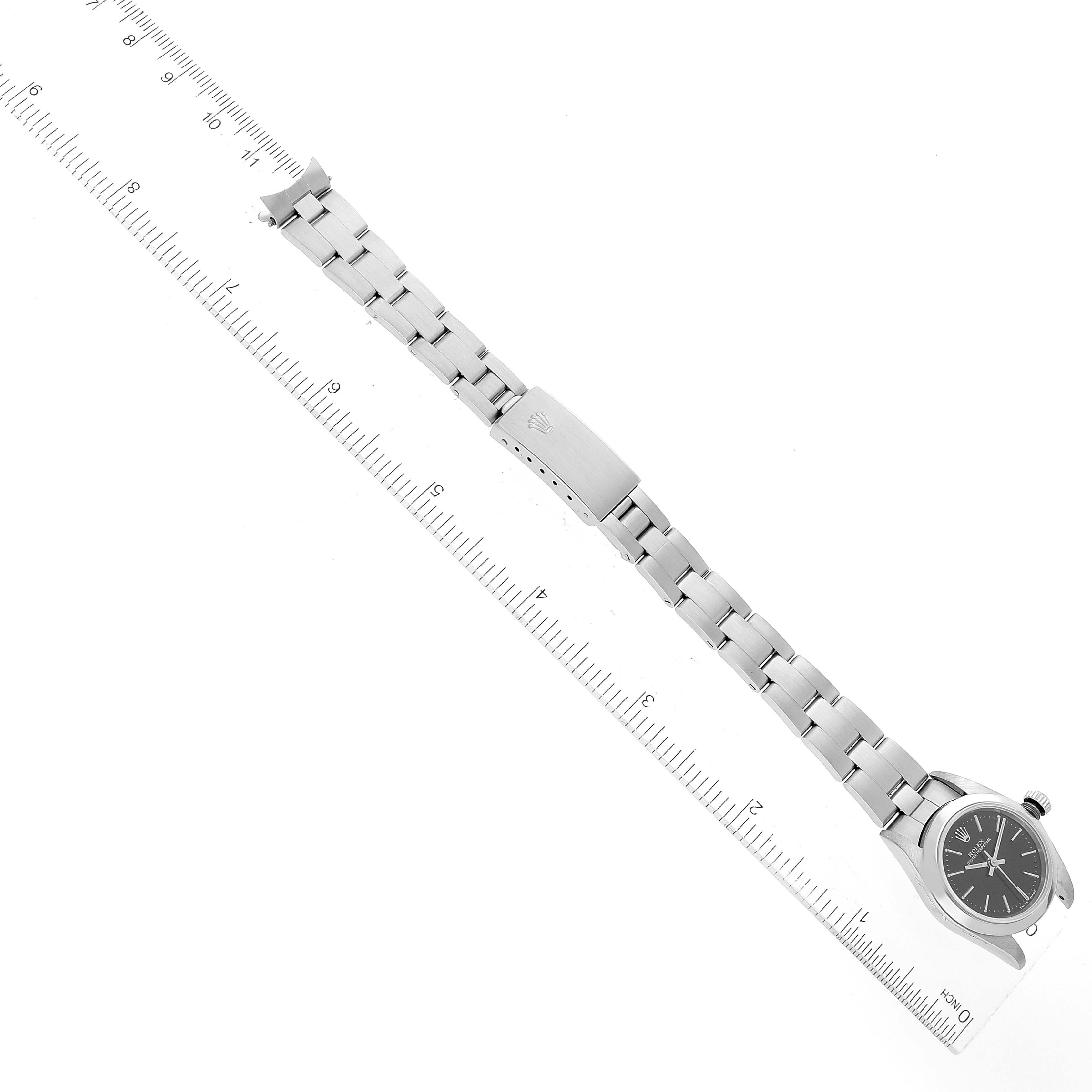 This image shows a top-down view of a Rolex Oyster Perpetual 76080 Women's Stainless Steel Black Dial 76080 Women's Stainless Steel Black Dial watch and its metal bracelet alongside a measuring ruler.