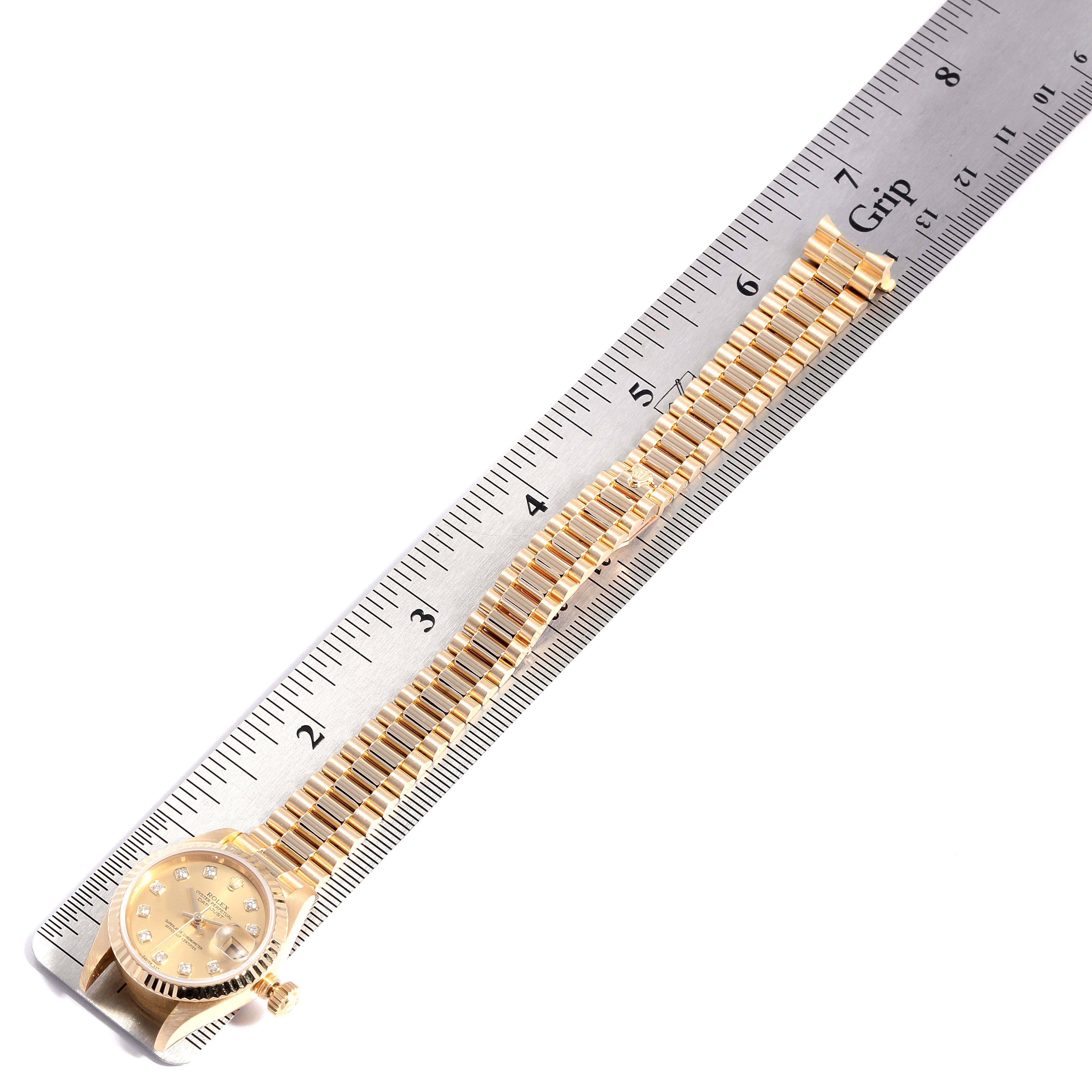 The Rolex President 79178  Women
s Yellow Gold Champagne Dial 79178  Women
s Yellow Gold Champagne Dial model watch is shown lying flat next to a ruler, displaying its dial and full gold bracelet.