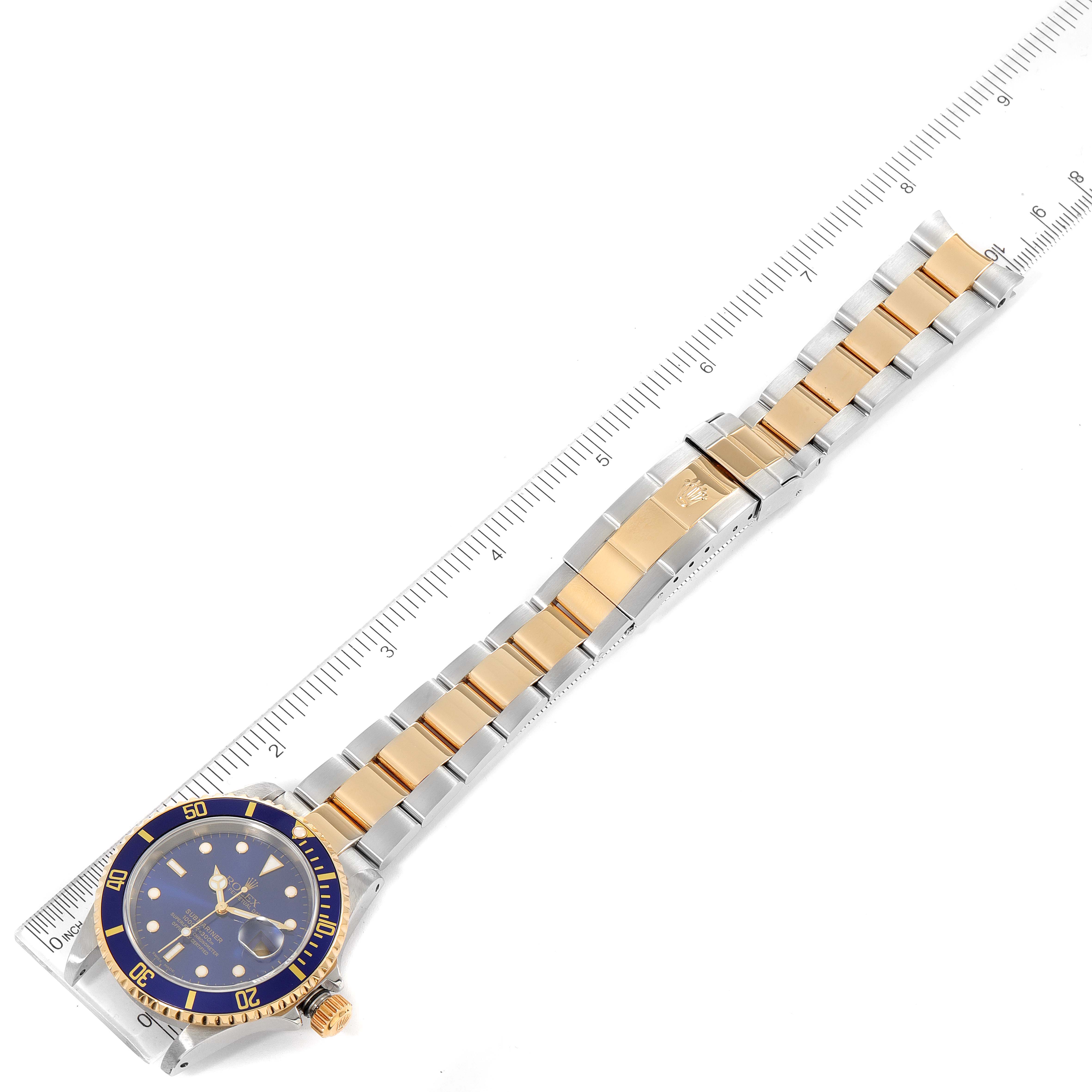 The image shows the Rolex Submariner 16613 Men
s Steel and Gold (two tone) Blue Dial 16613 Men
s Steel and Gold (two tone) Blue Dial watch laid flat with a ruler alongside, highlighting its full bracelet and face.