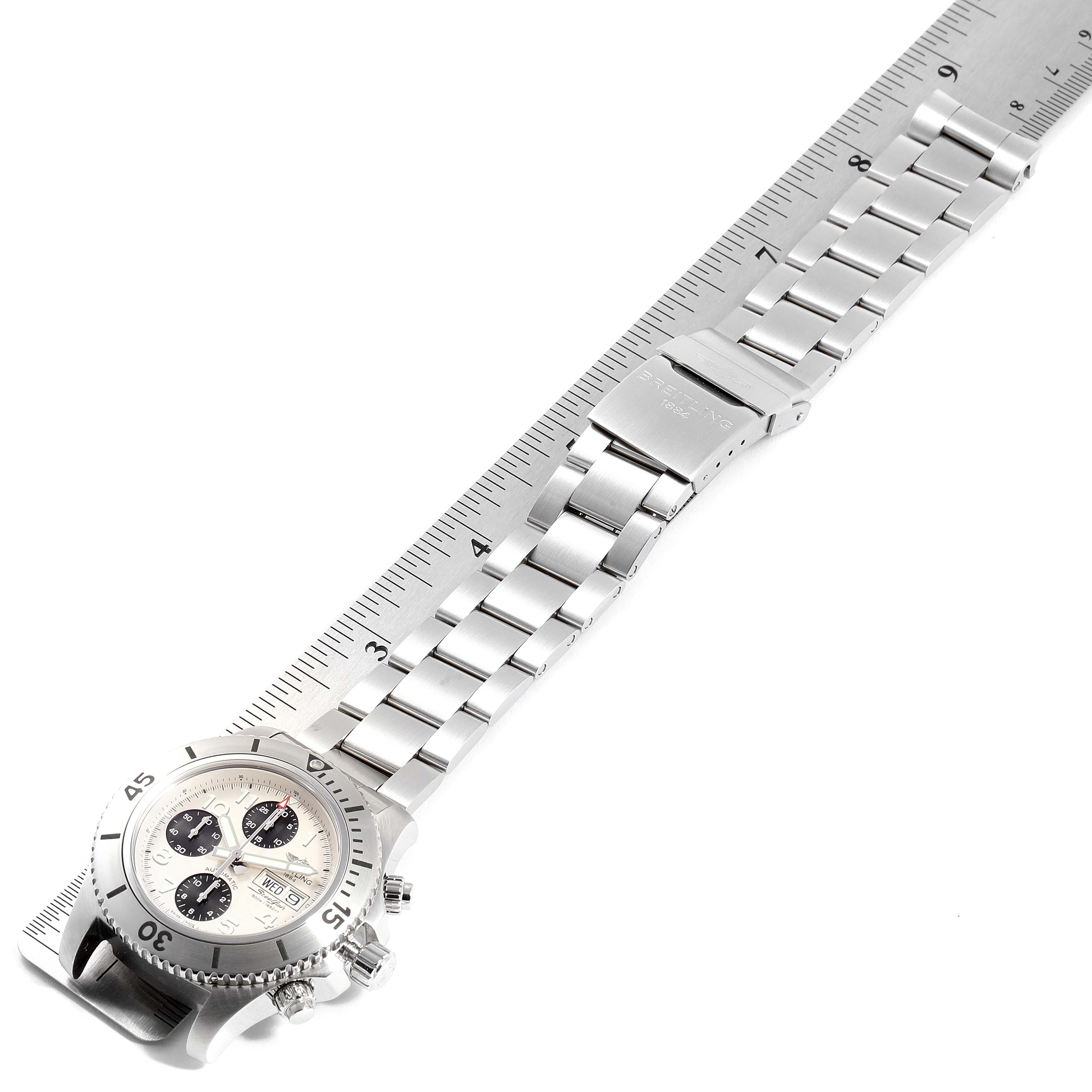 The image shows a side angle of the Breitling Superocean A13341C3/BD19 Men's Stainless Steel White Dial A13341C3/BD19 Men's Stainless Steel White Dial watch, highlighting the dial, bezel, and metal bracelet with a ruler for scale.
