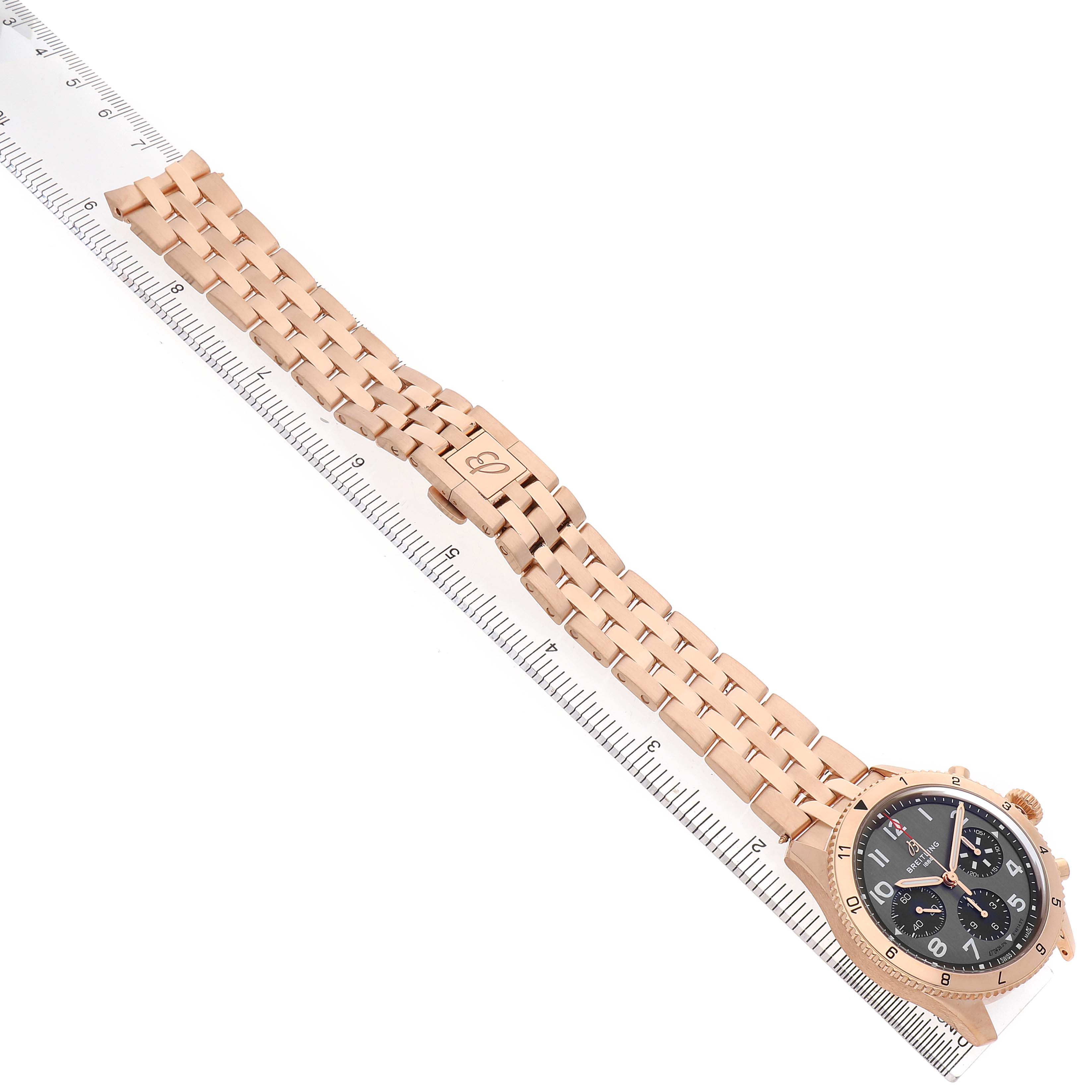 The Breitling Aviator R23380 Men's Rose Gold Grey Dial watch is shown facing upward, highlighting the face, case, and full bracelet with a ruler for scale.