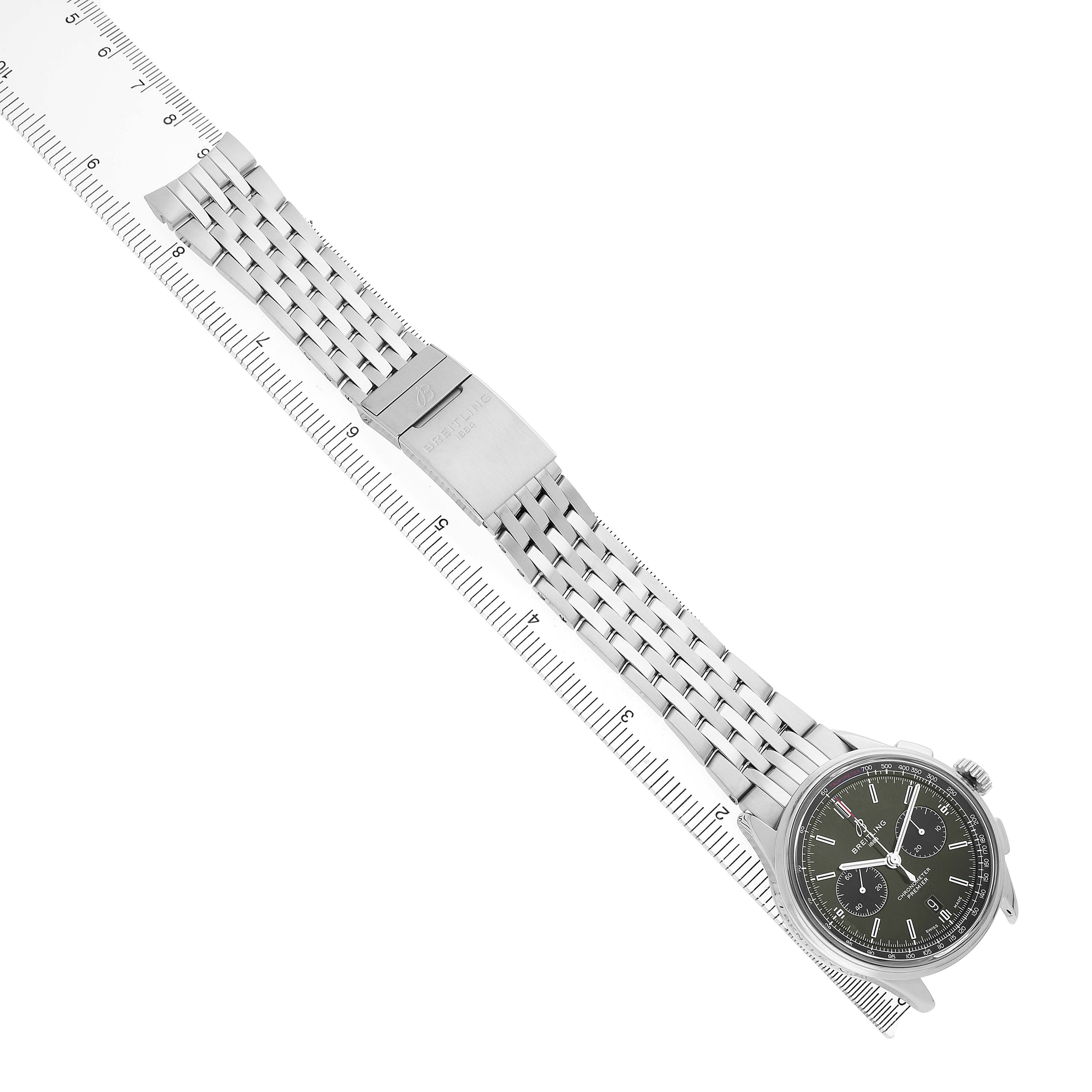 The Breitling Premier AB0118 Men's Stainless Steel Green Dial watch is shown from a top-down angle highlighting the dial, metal bracelet, and clasp alongside a ruler for scale.