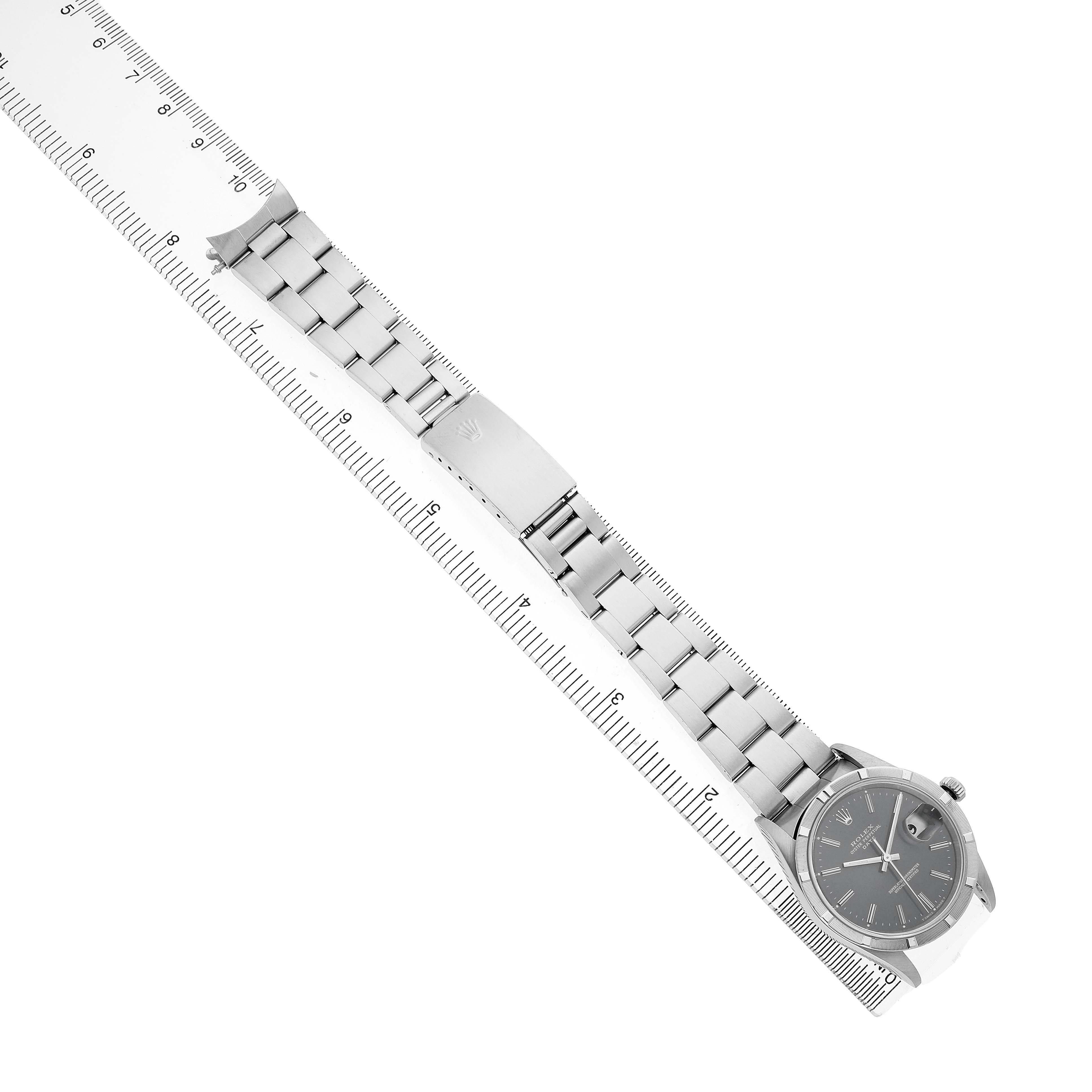 The Rolex Date 15210 Men's Stainless Steel Blue Dial watch is shown from a top-down angle, displaying the face, bracelet, and clasp alongside a ruler for scale.