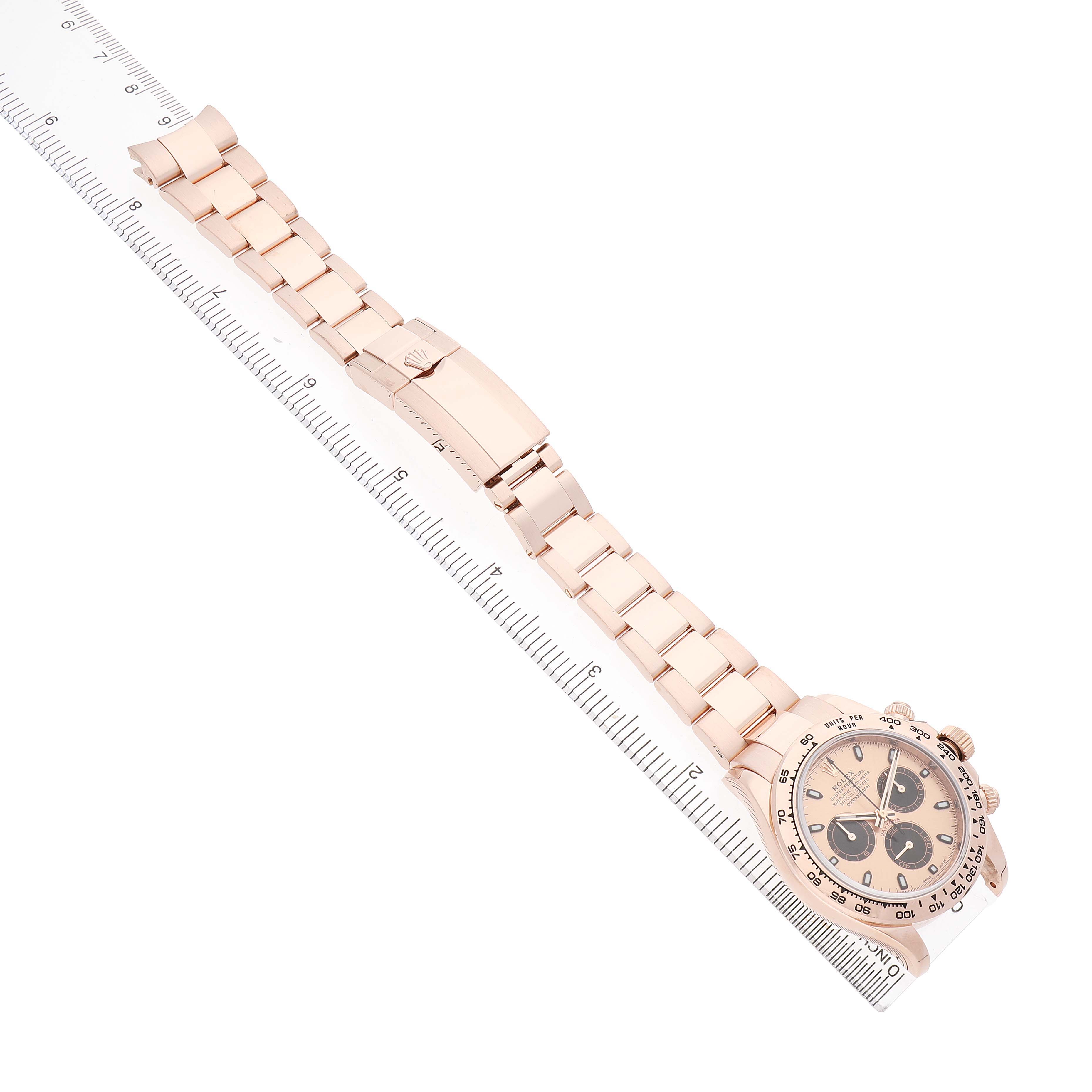 The image shows a Rolex Daytona 116505 Men's Rose Gold Pink Dial watch placed diagonally, highlighting the bracelet, clasp, and face against a ruler.