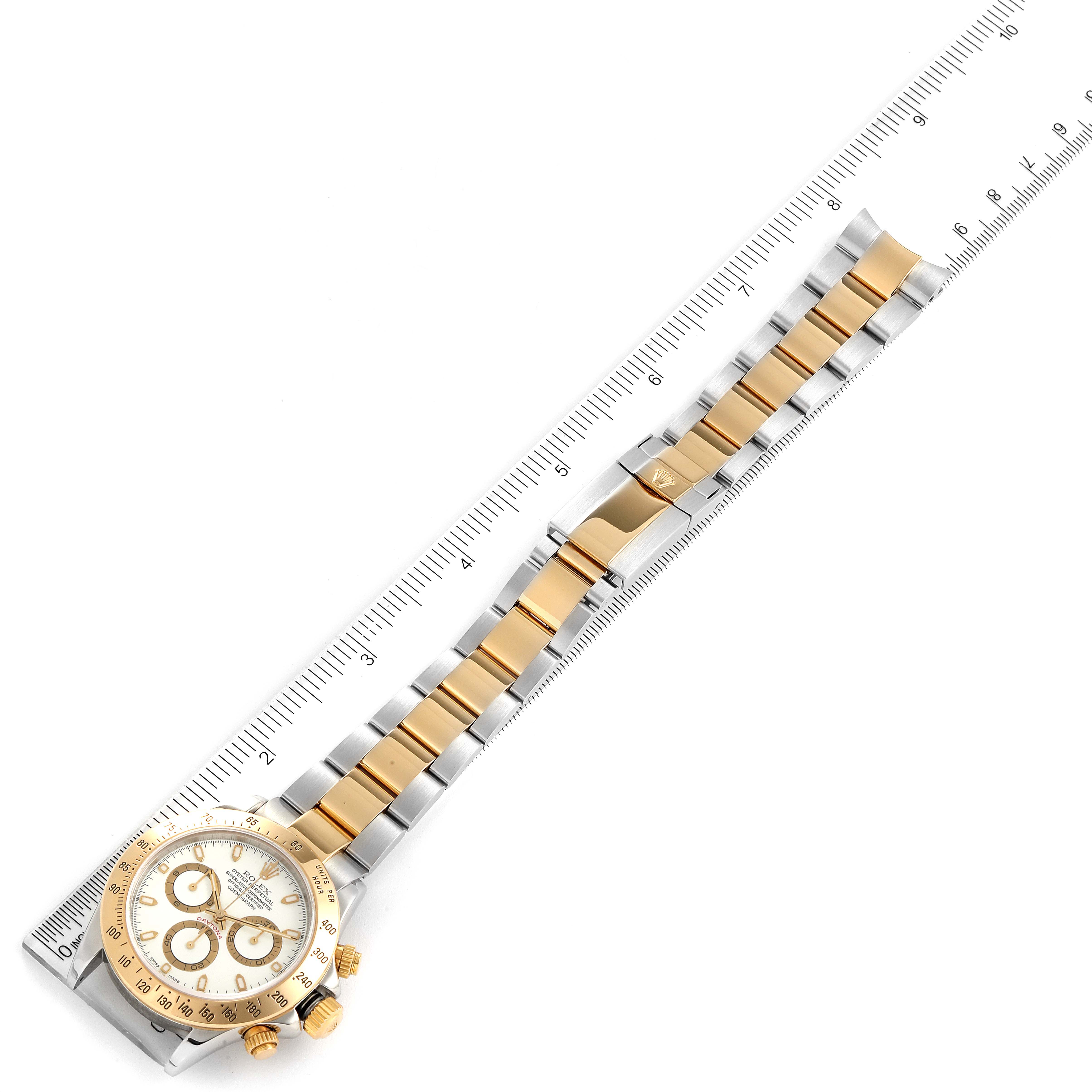 The image shows a Rolex Daytona 116523 Men
s Steel and Gold (two tone) White Dial 116523 Men
s Steel and Gold (two tone) White Dial watch laid flat against a ruler, displaying the face, bezel, and full bracelet.
