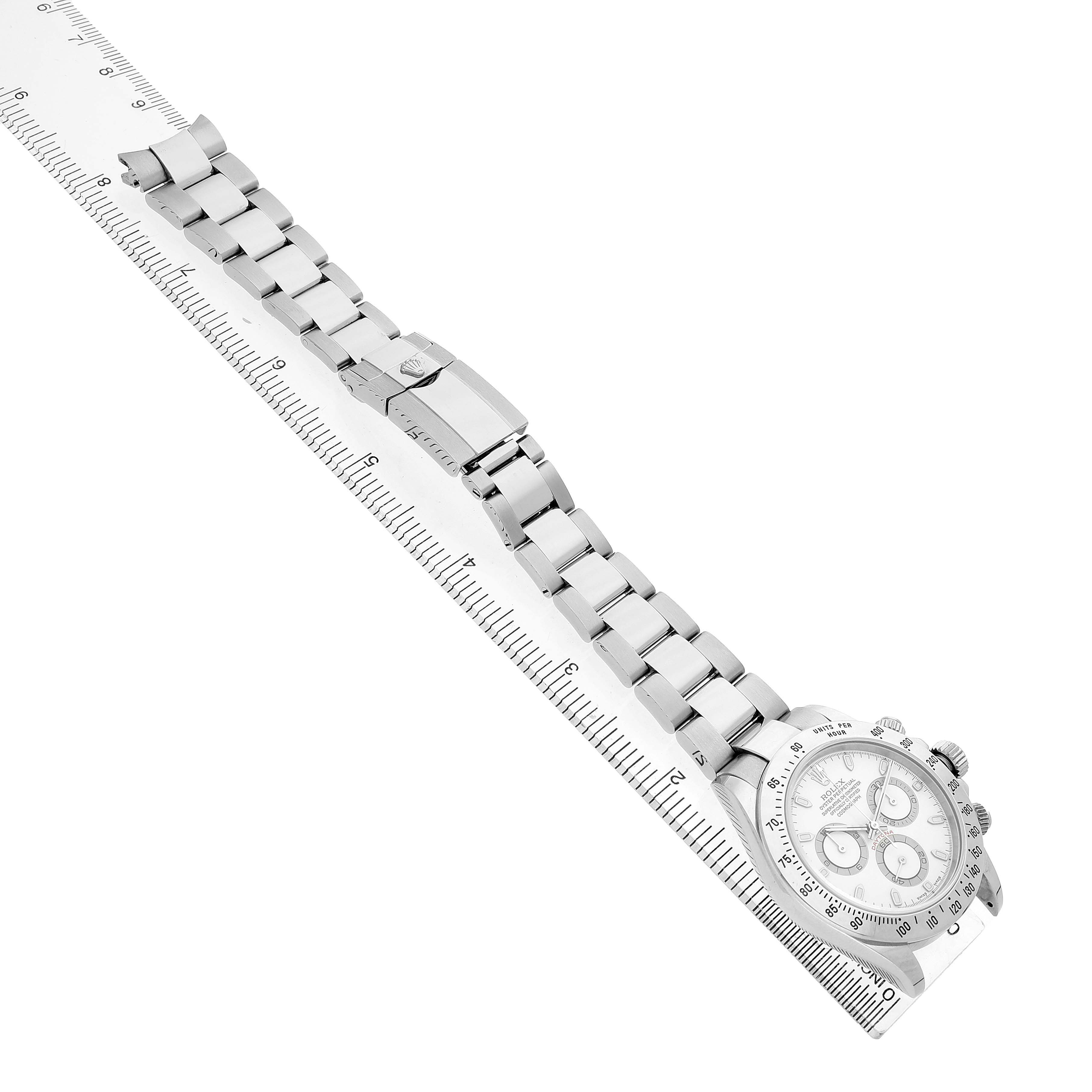 The Rolex Daytona 116520 Men's Stainless Steel White Dial watch is shown diagonally with a focus on its bracelet and clasp, alongside a ruler for scale.