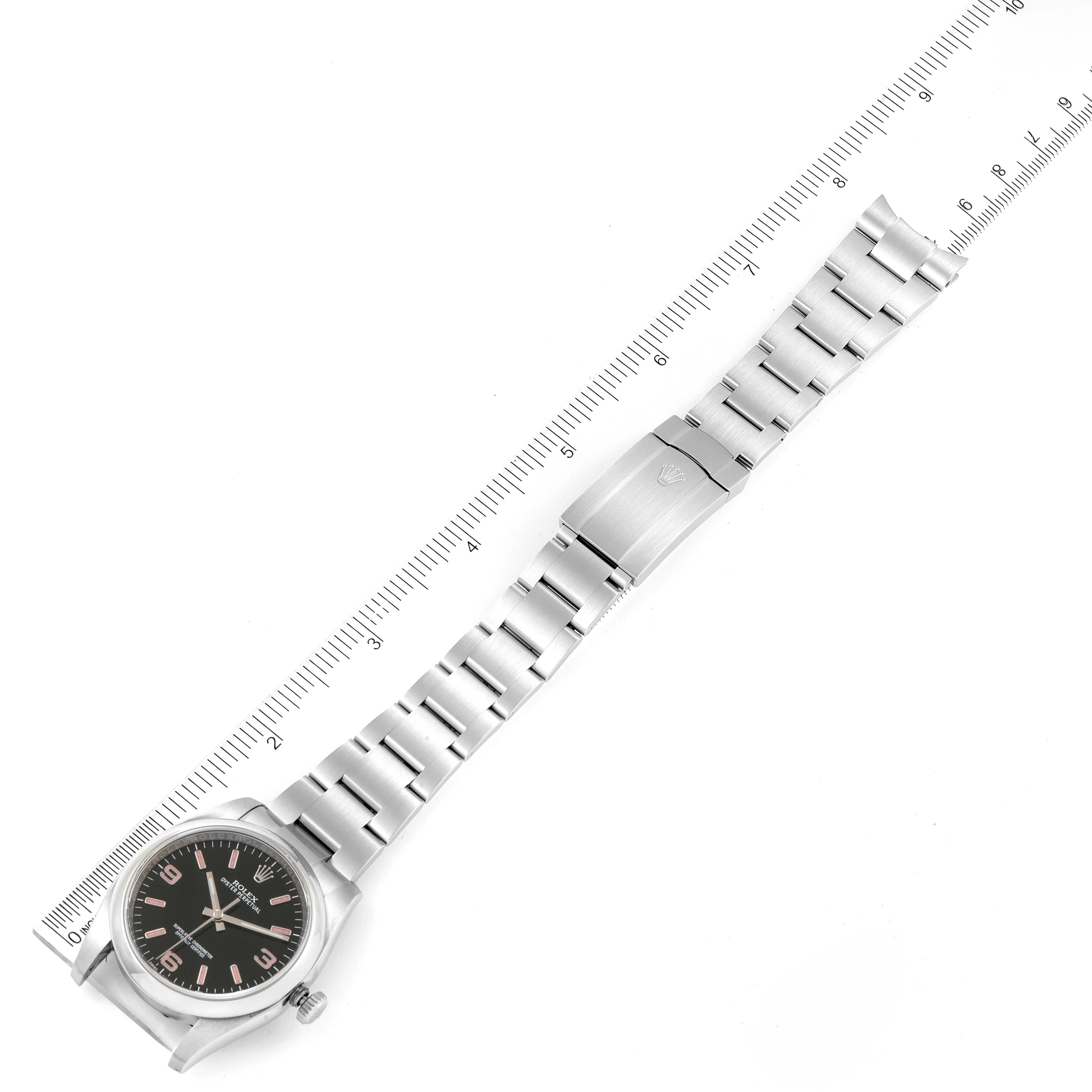 The image shows a top-down view of a Rolex Oyster Perpetual 116000 Men
s Stainless Steel Black Dial 116000 Men
s Stainless Steel Black Dial watch with its full stainless steel bracelet extended alongside a ruler.