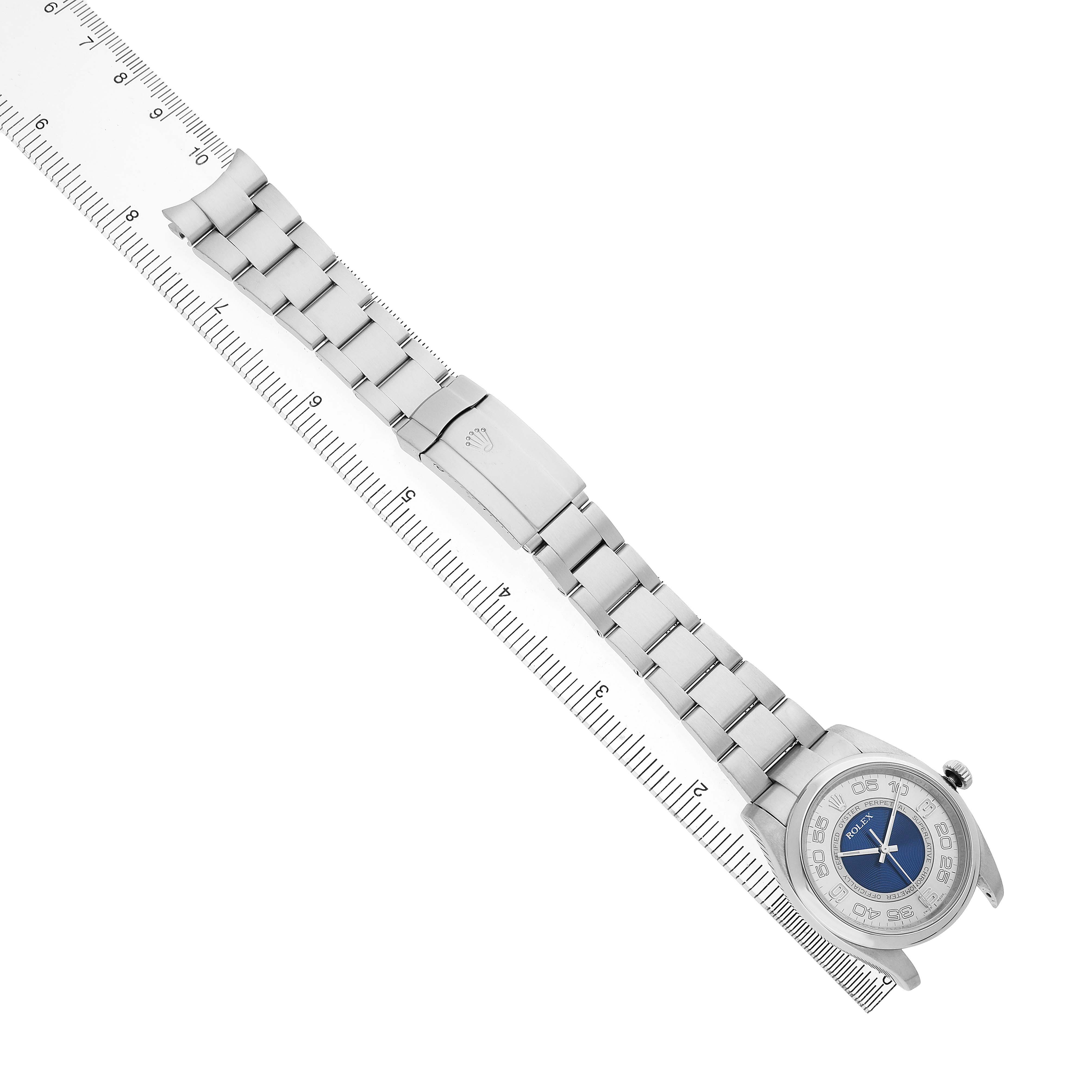 The Rolex Oyster Perpetual 116000 Men's Stainless Steel Silver Dial is shown diagonally, highlighting the bracelet, clasp, and part of the dial with a ruler for scale.