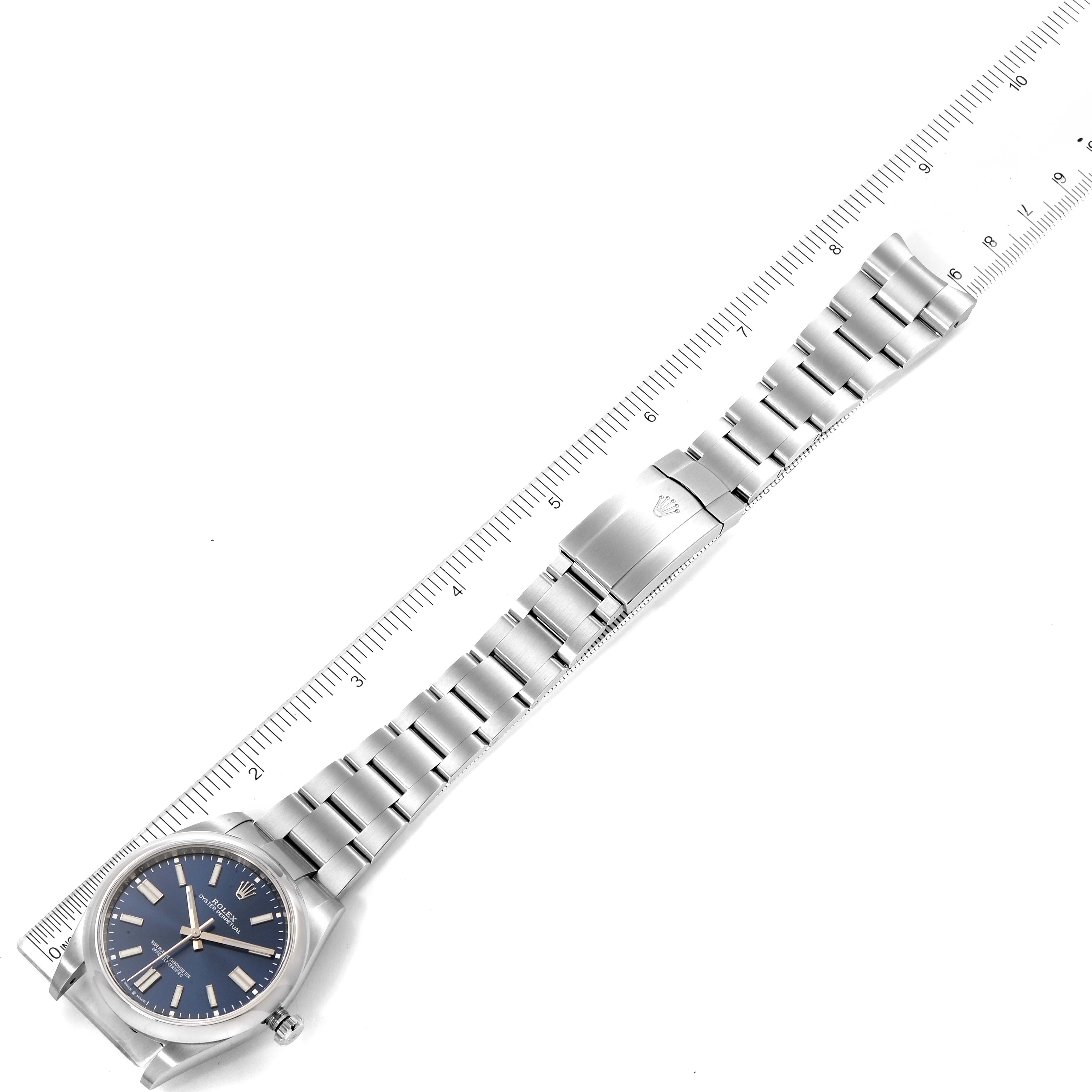 The image shows a top-down view of a Rolex Oyster Perpetual 124300 Men
s Stainless Steel Blue Dial 124300 Men
s Stainless Steel Blue Dial watch and its metal bracelet next to a ruler for scale.