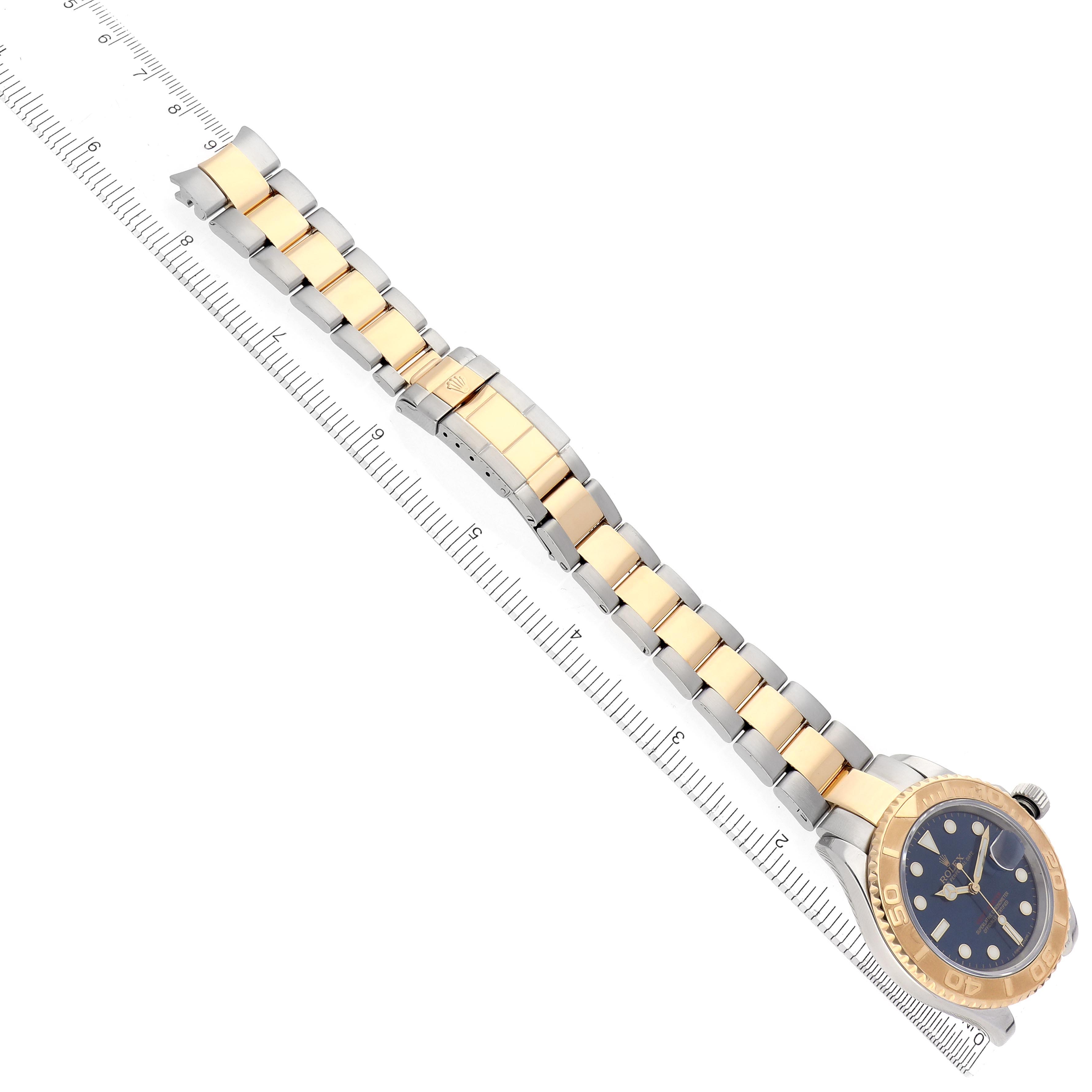 The Rolex Yacht-Master 16623 Men
s Steel and Gold (two tone) Blue Dial 16623 Men
s Steel and Gold (two tone) Blue Dial watch is shown from a top angle, displaying its gold and silver bracelet and the watch face beside a ruler.